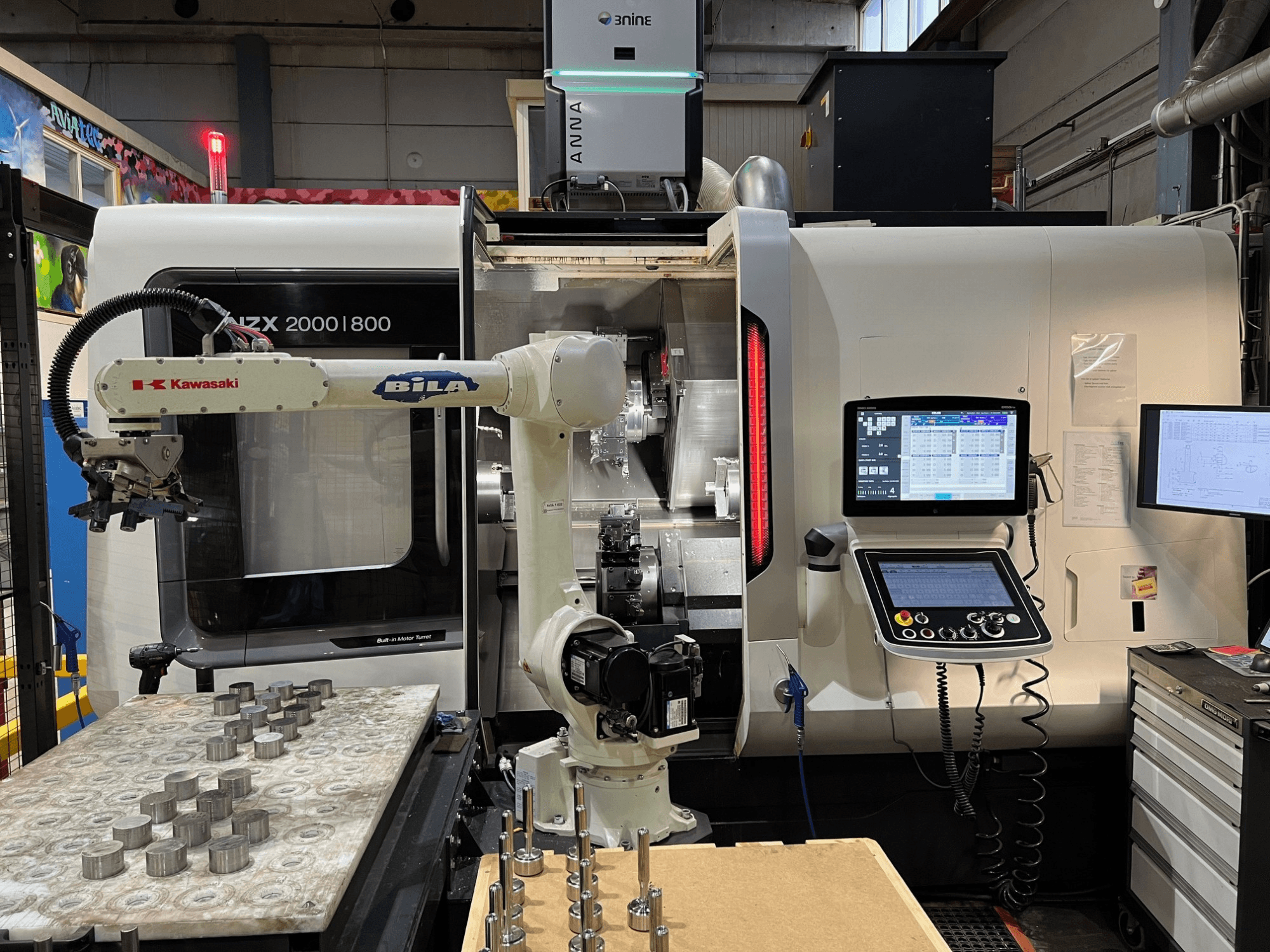 Горизонтальный токарный станок DMG MORI NZX 2000/800SY в цехе; на снимке видны манипулятор Kawasaki и пульт управления.