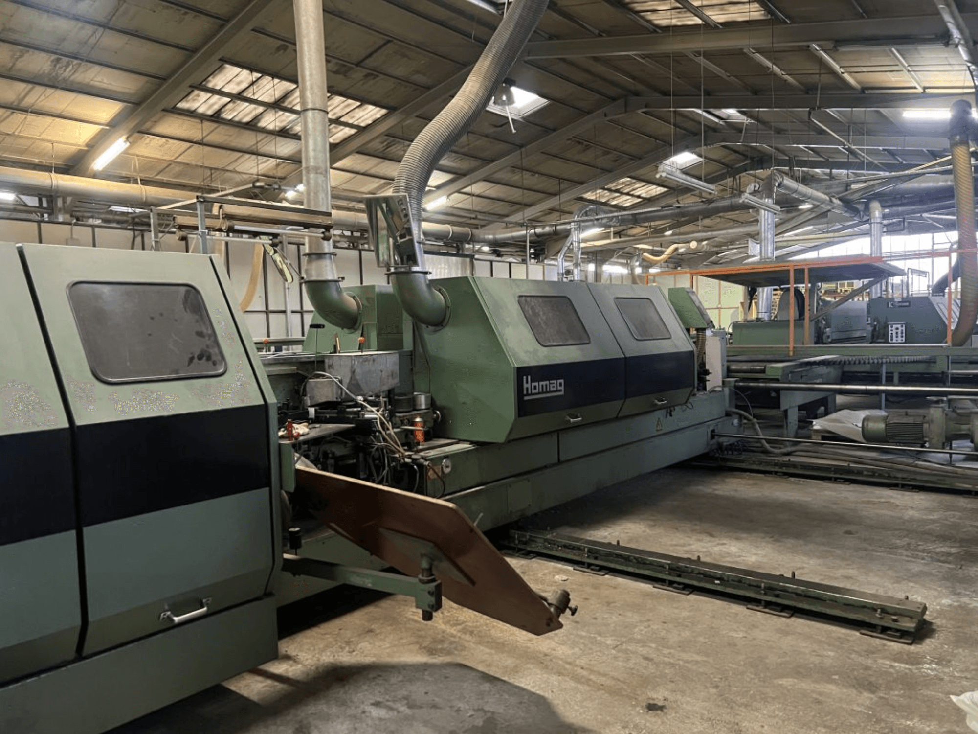 Промышленная машина Homag зеленого цвета, вид сбоку, с рабочими компонентами и панелью управления на складе.