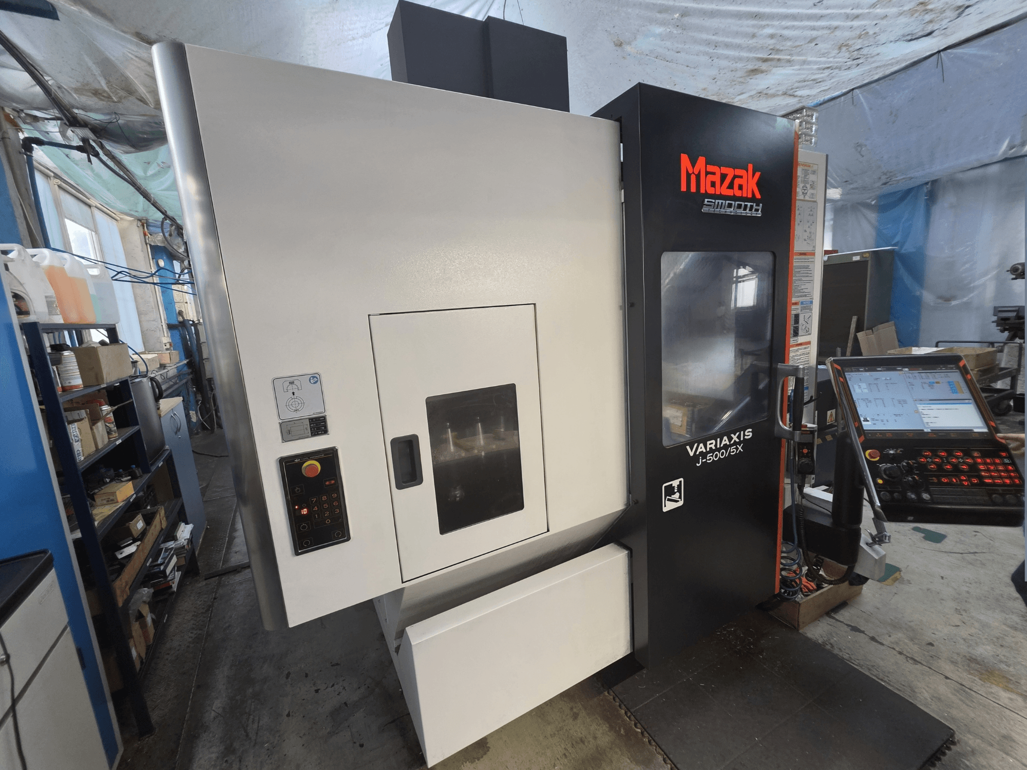 Вертикальный обрабатывающий центр Mazak VARIAXIS J-500/5X в виде спереди, с панелью управления и большим окном обзора рабочей зоны.