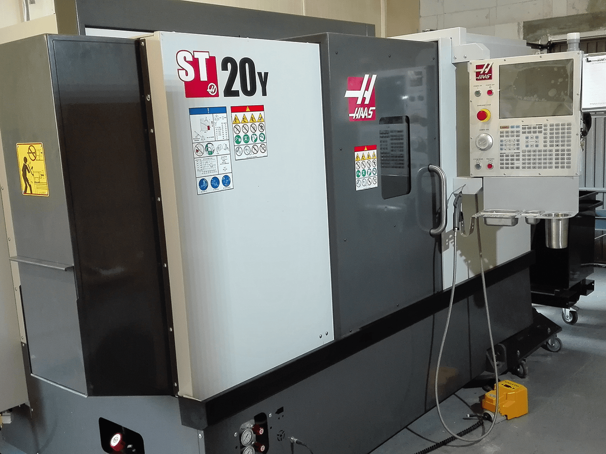 Токарный станок с ЧПУ Haas ST20Y (вид спереди), панель управления, знаки безопасности и система подачи охлаждающей жидкости.