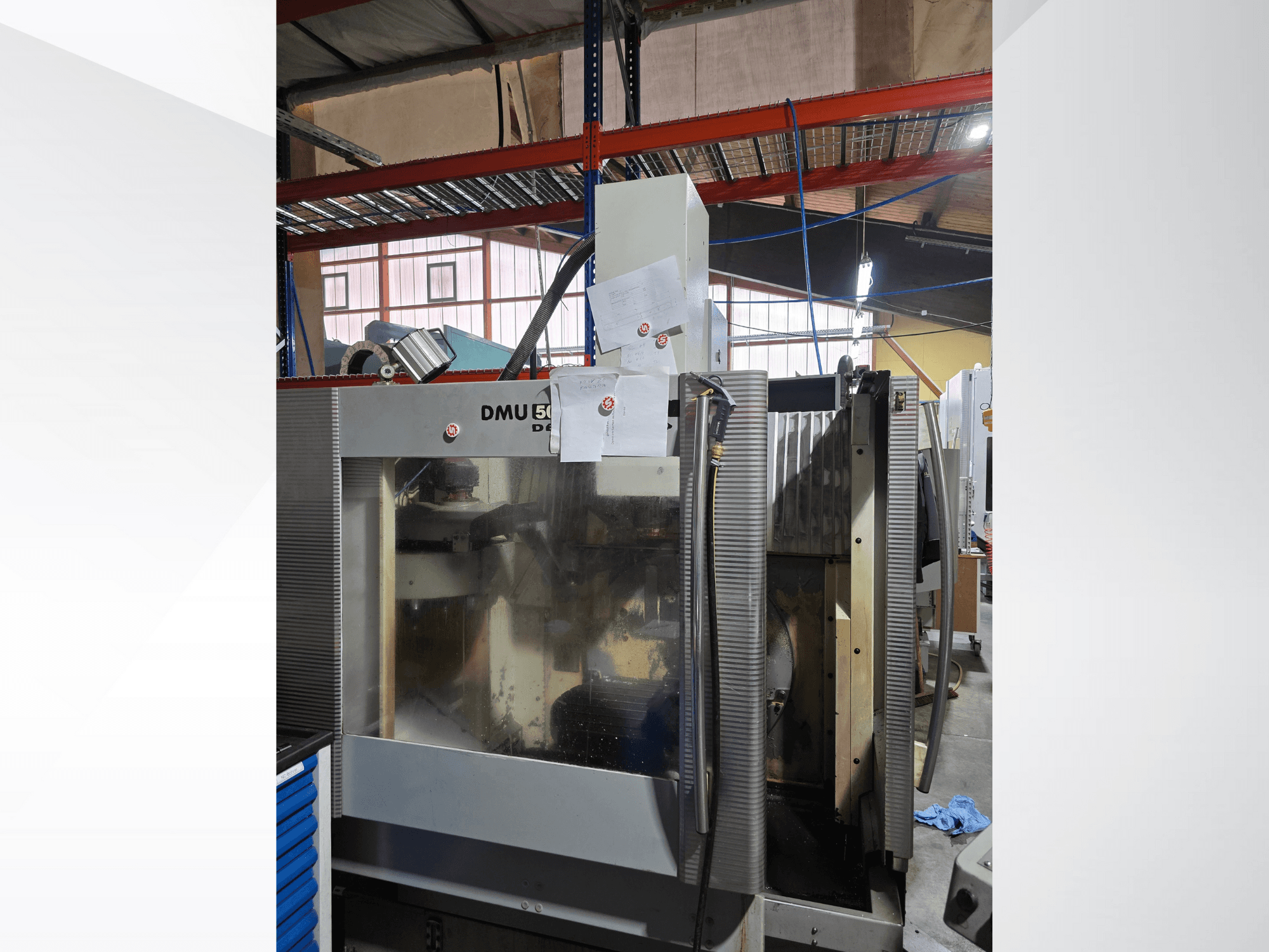 Трехкоординатный обрабатывающий центр с ЧПУ DMU 50 в мастерской, показан спереди, демонстрирует рабочие компоненты и прилагаемые документы.
