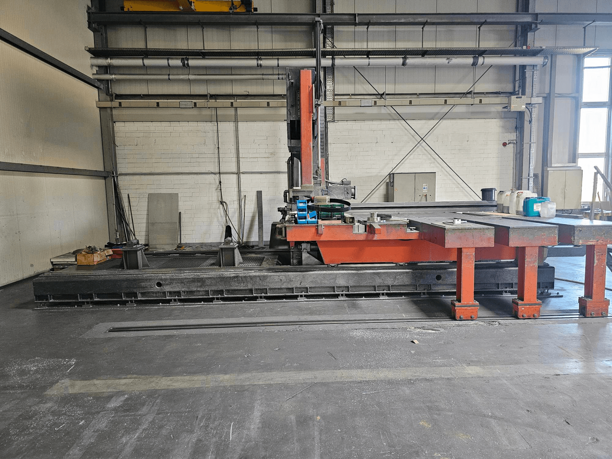 Промышленный станок для резки в открытой мастерской, оранжевый и черный, с большим столом; вид сбоку, показывающий принадлежности и рабочее пространство.