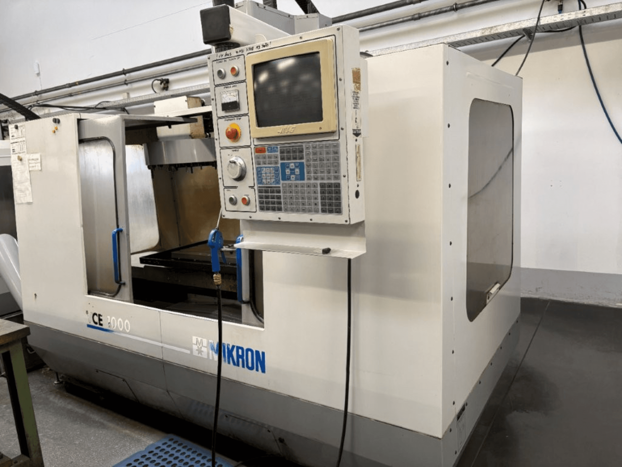 Станок с ЧПУ Mikron CE 2000, вид спереди; панель управления с кнопками и экраном, серебристая внешняя поверхность и рабочая зона.
