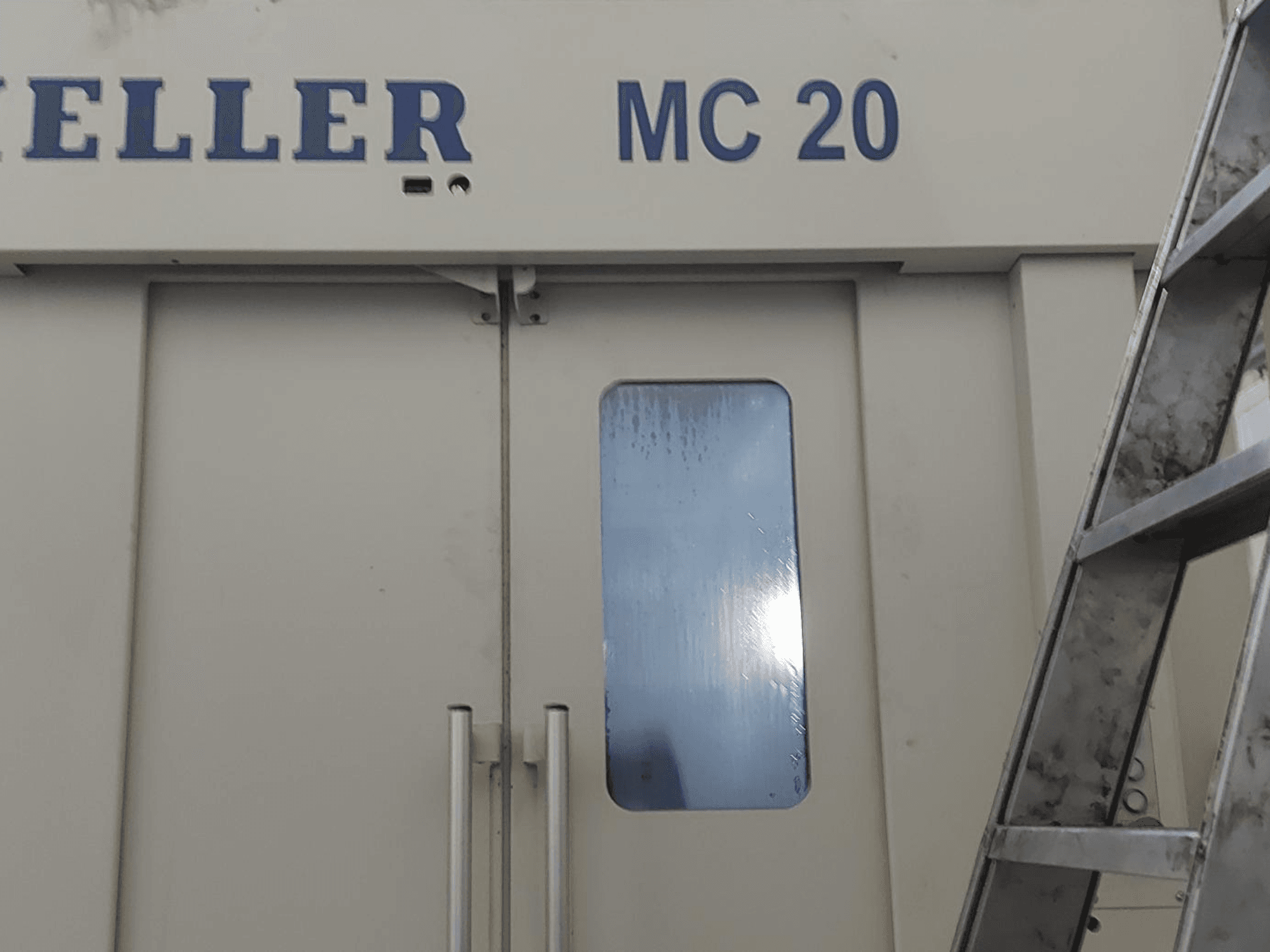 Вид спереди горизонтального обрабатывающего центра HELLER MC 20, видны дверные ручки и небольшое окно. Лестница сбоку.