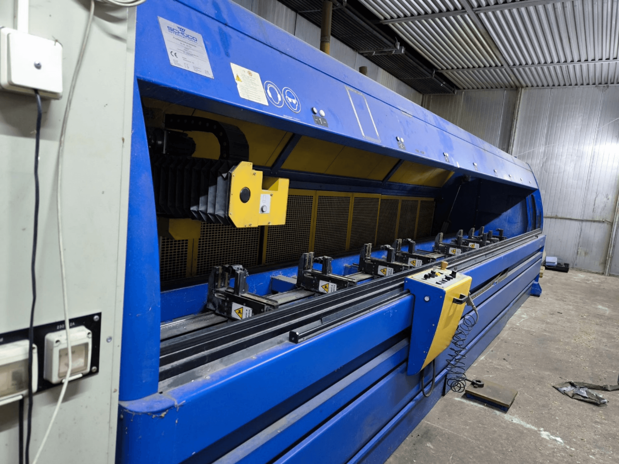 Промышленный раскройный станок Schneider синего цвета, вид сбоку, видны панель управления, ремни и несколько станций зажима.