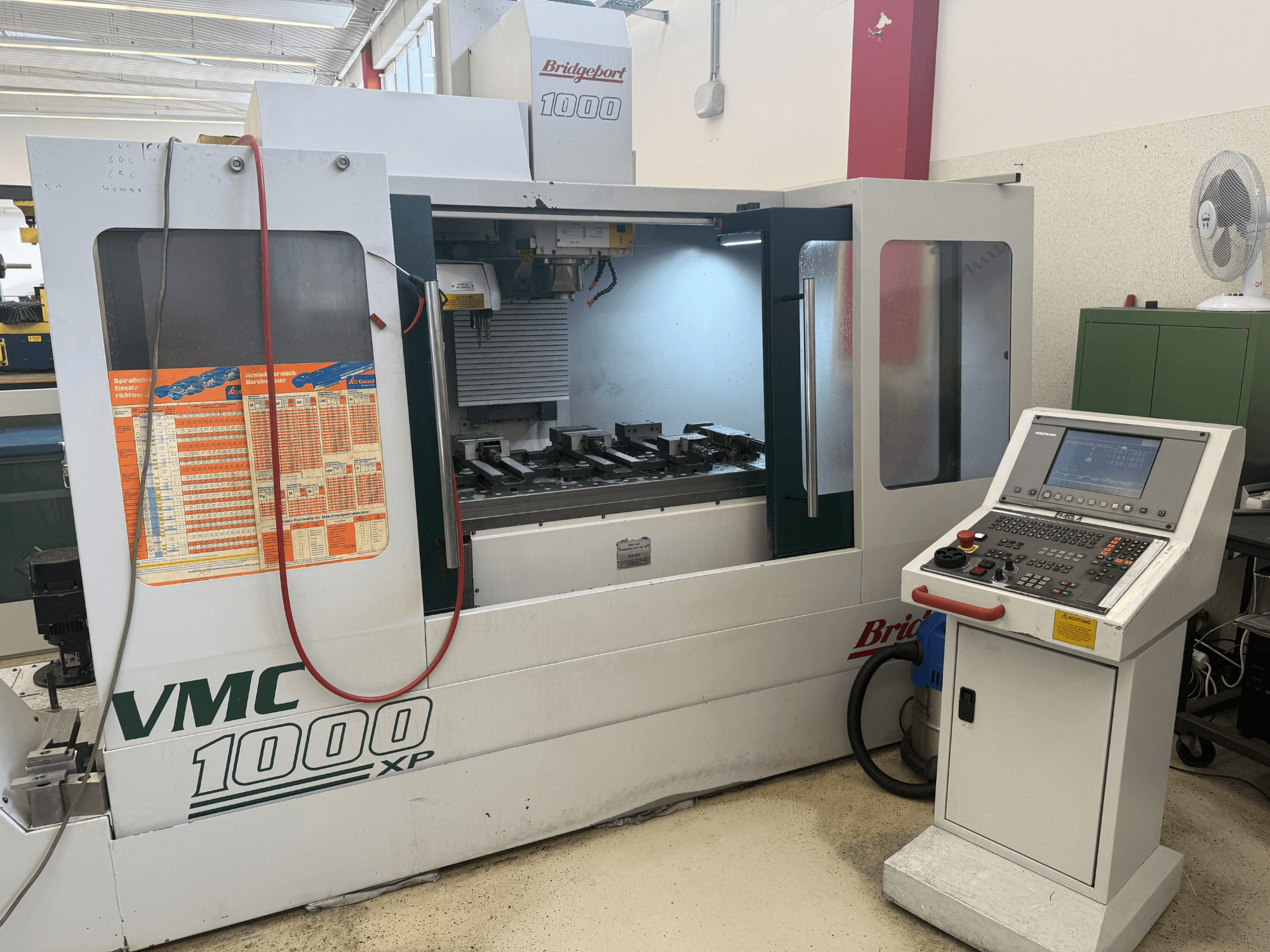 Вид спереди на вертикальный обрабатывающий центр Bridgeport VMC 1000 XP с изображением панелей управления, рабочей зоны и держателей инструментов.