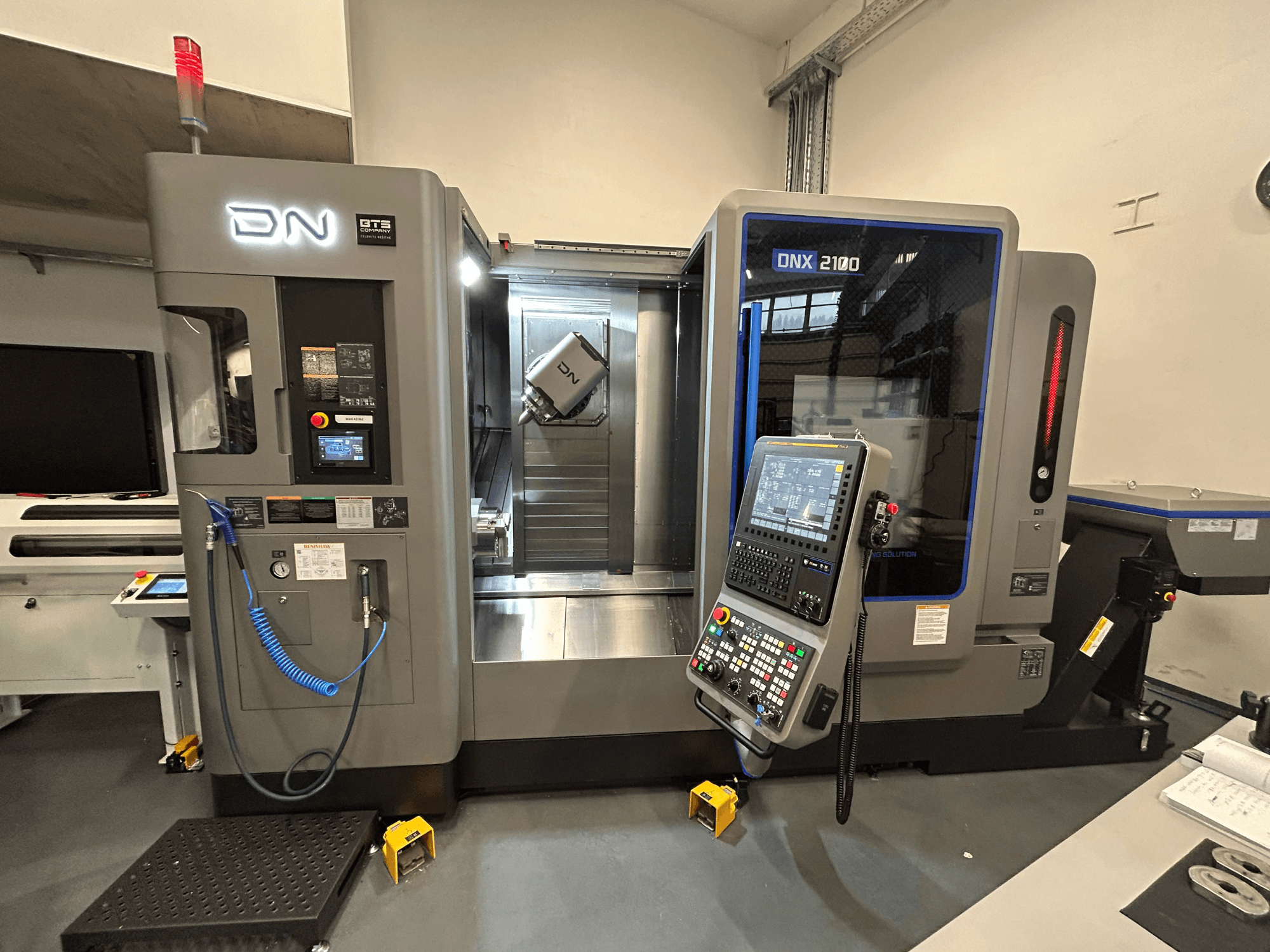Станок с ЧПУ DN ONX 2100, вид спереди, панель управления, рабочая зона и инструмент. Оснащен светом безопасности и индикаторами работы.