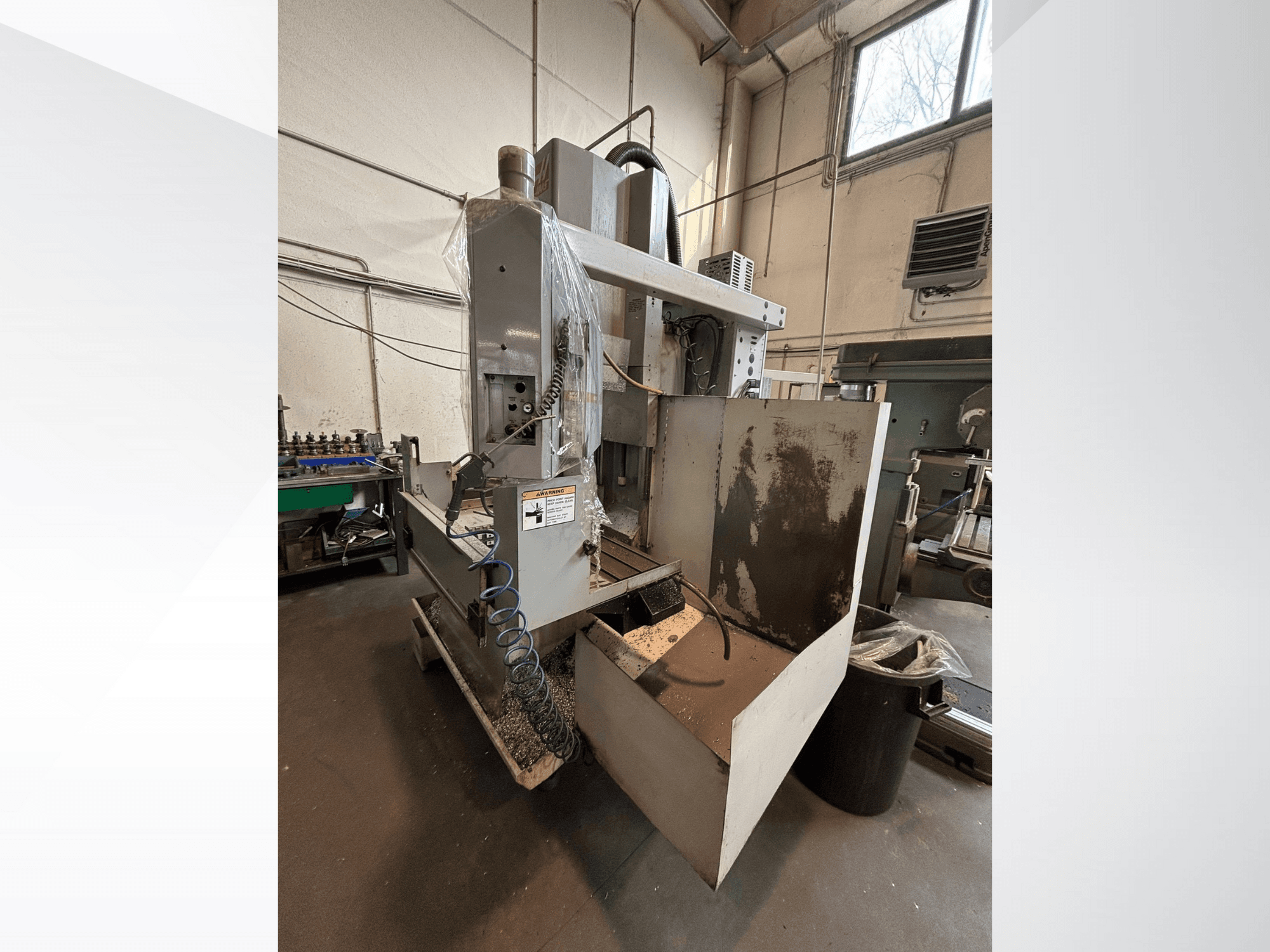 Вертикальный фрезерный станок с защитным кожухом, вид сбоку; видны шланг подачи охлаждающей жидкости и панель управления. Идеально подходит для обработки.