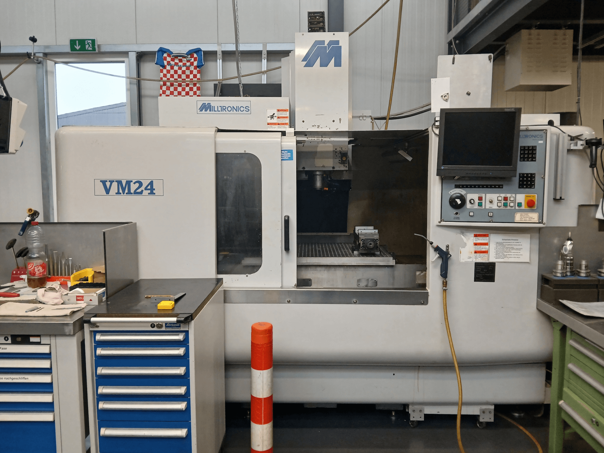 Фрезерный станок с ЧПУ Milltronics VM24, показанный спереди, с панелью управления, хранилищем инструментов и рабочей зоной.