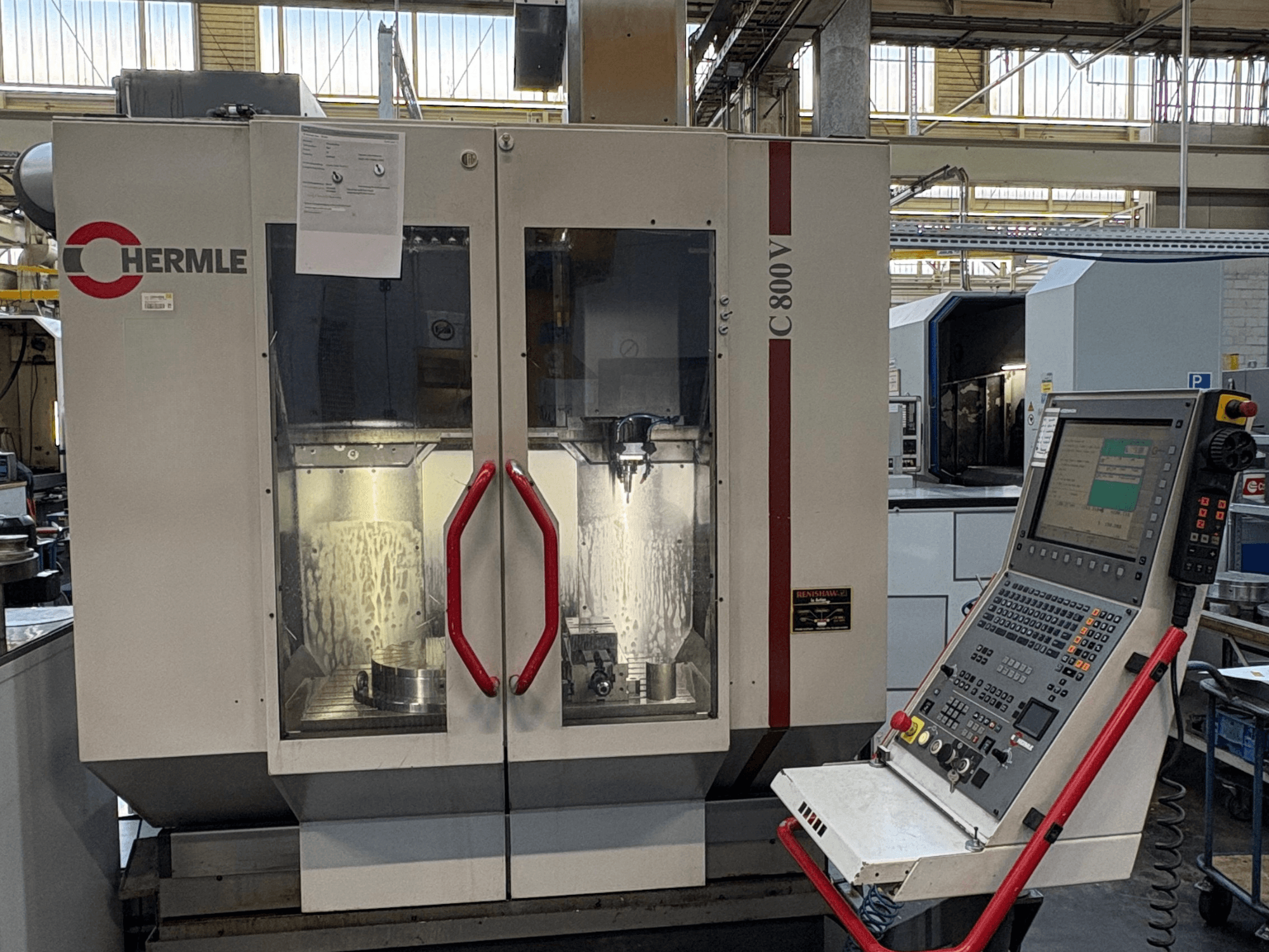 Вертикальный обрабатывающий центр HERMLE C 800 V, вид спереди, с дверцами с красными ручками и панелью управления справа.