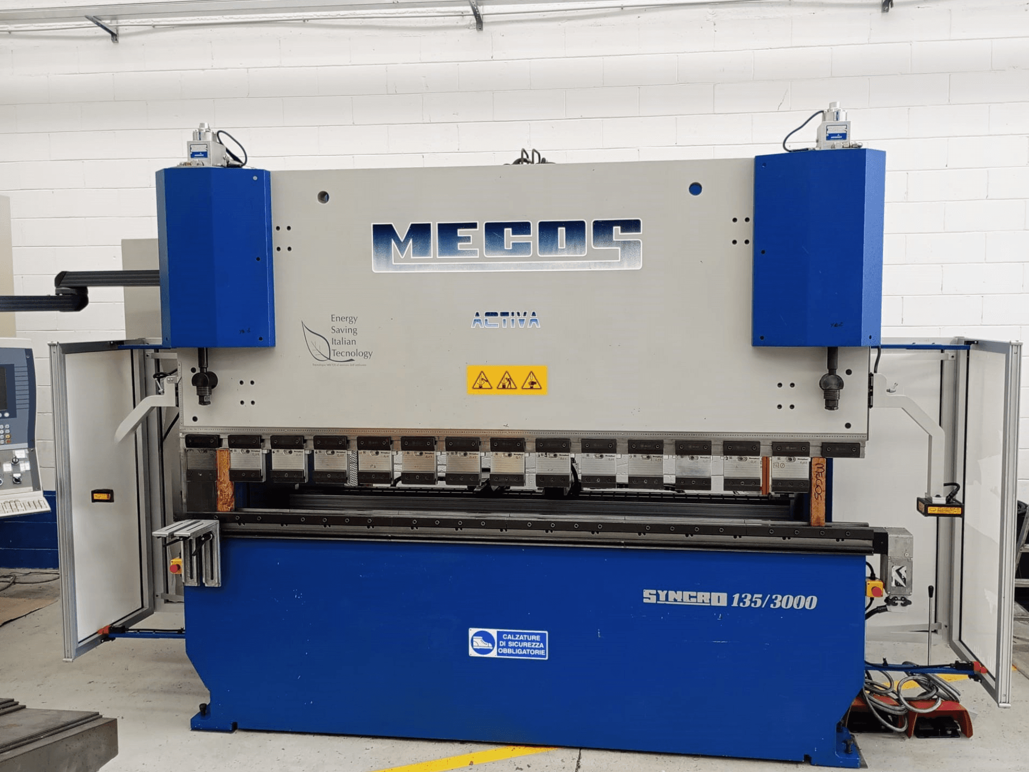 Вид спереди листогибочного пресса MECOS SYNCRO 135/3000, демонстрирующий органы управления, гибочные инструменты и функции безопасности.