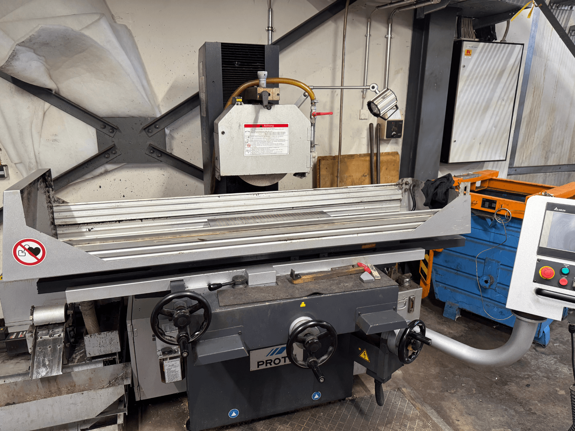 Машина PROTEC, вид спереди, изображающий плоскошлифовальную машину с ручным управлением, предупреждениями о безопасности и системой охлаждения.