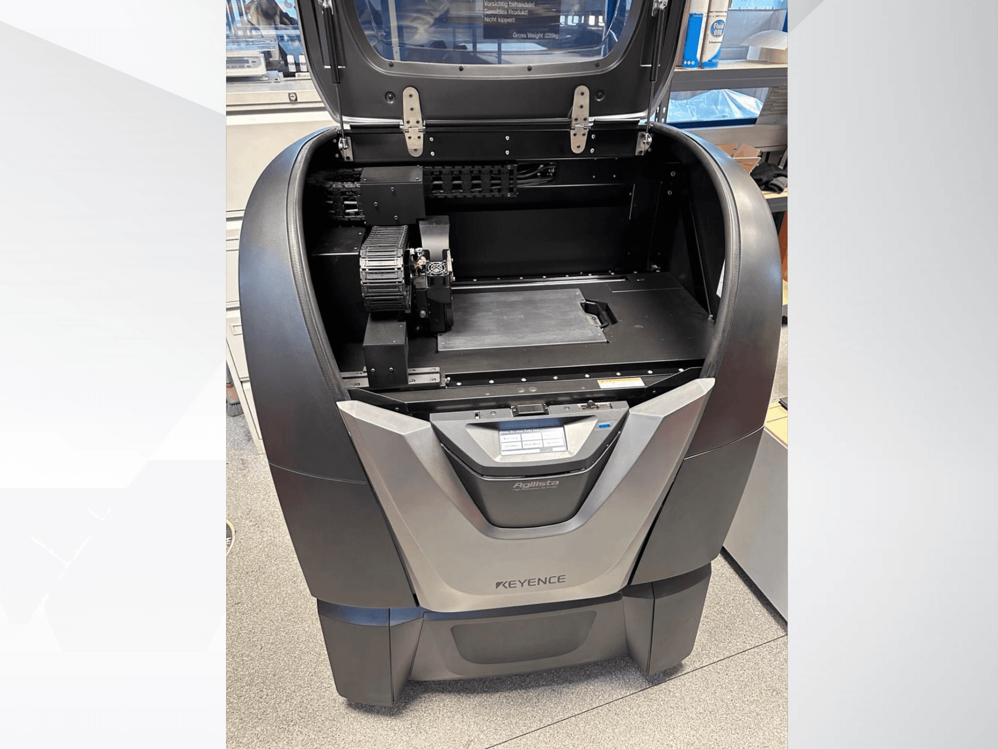 3D-принтер KEYENCE Agilista, вид спереди, демонстрирует открытую верхнюю часть, большую платформу для сборки и внутренние механические компоненты.