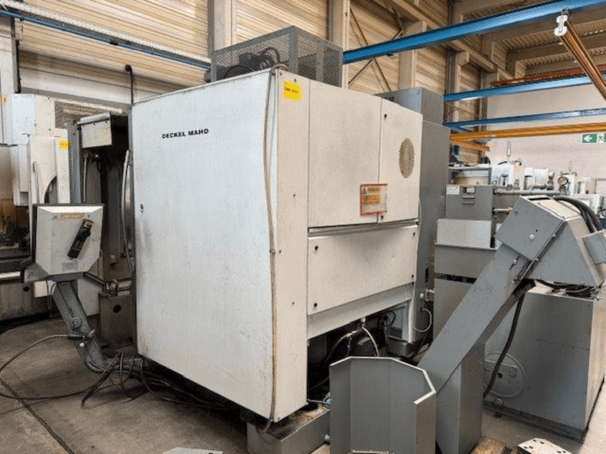 Вертикальный обрабатывающий центр DECKEL MAHO DMC 100 V, вид сбоку, видна панель управления и различные приспособления.