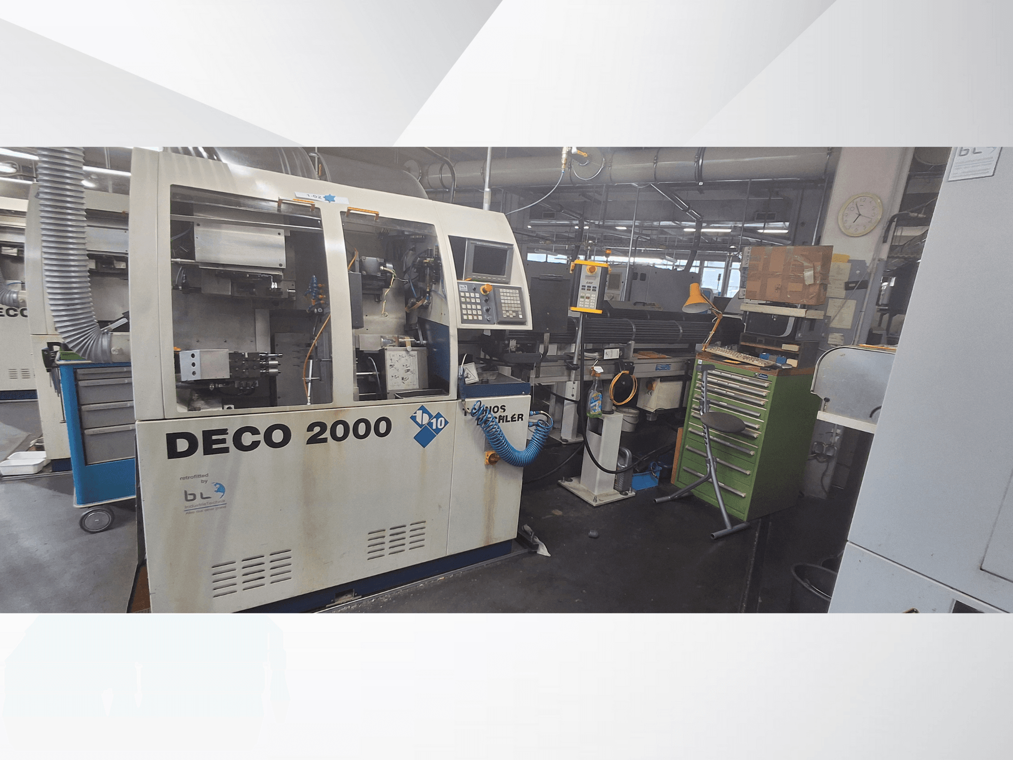 Станок DECO 2000 спереди: панель управления, трубы и загроможденное инструментами и коробками рабочее место.