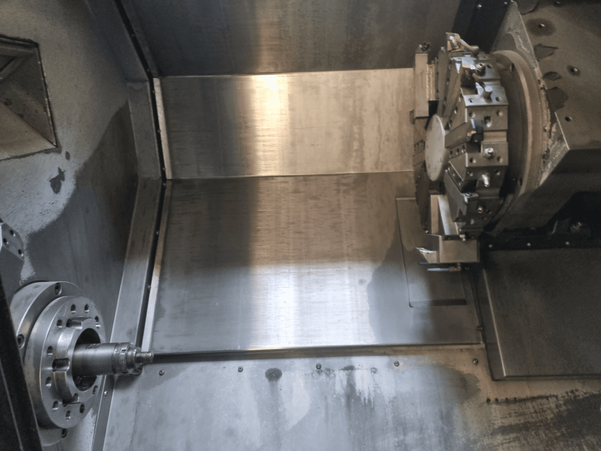 Вид изнутри на токарный станок с ЧПУ с вращающимся шпинделем и металлической рабочей поверхностью, демонстрирующий промышленное точное машиностроение.