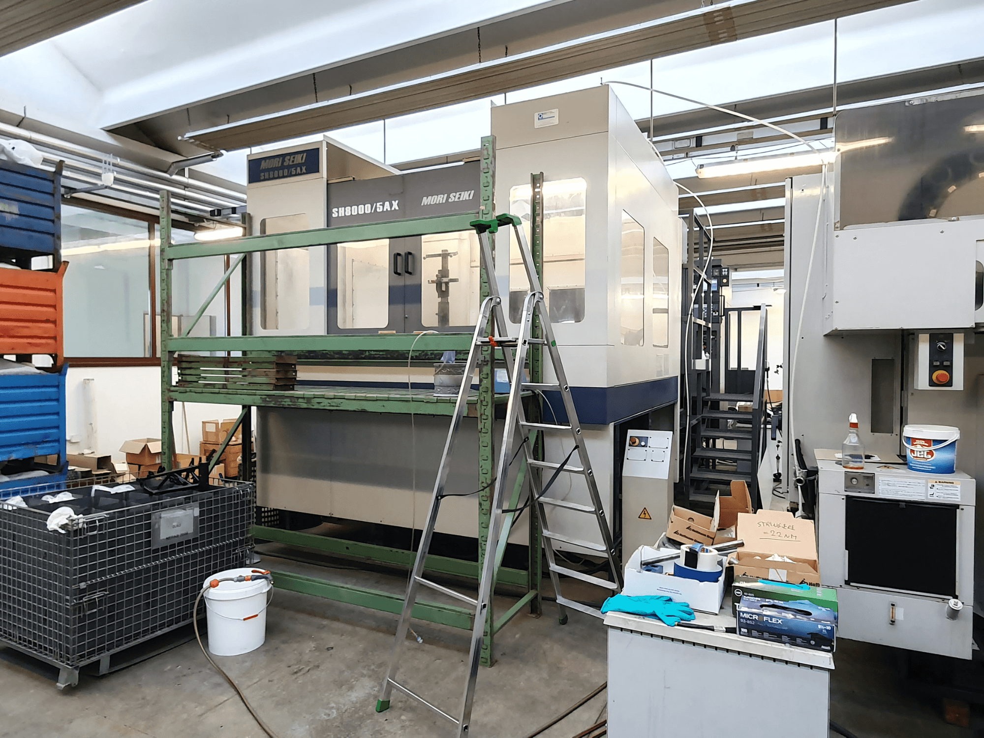 Станок с ЧПУ Mori Seiki SH-8000/5AX в мастерской, вид спереди, рядом инструменты и ящики для хранения.