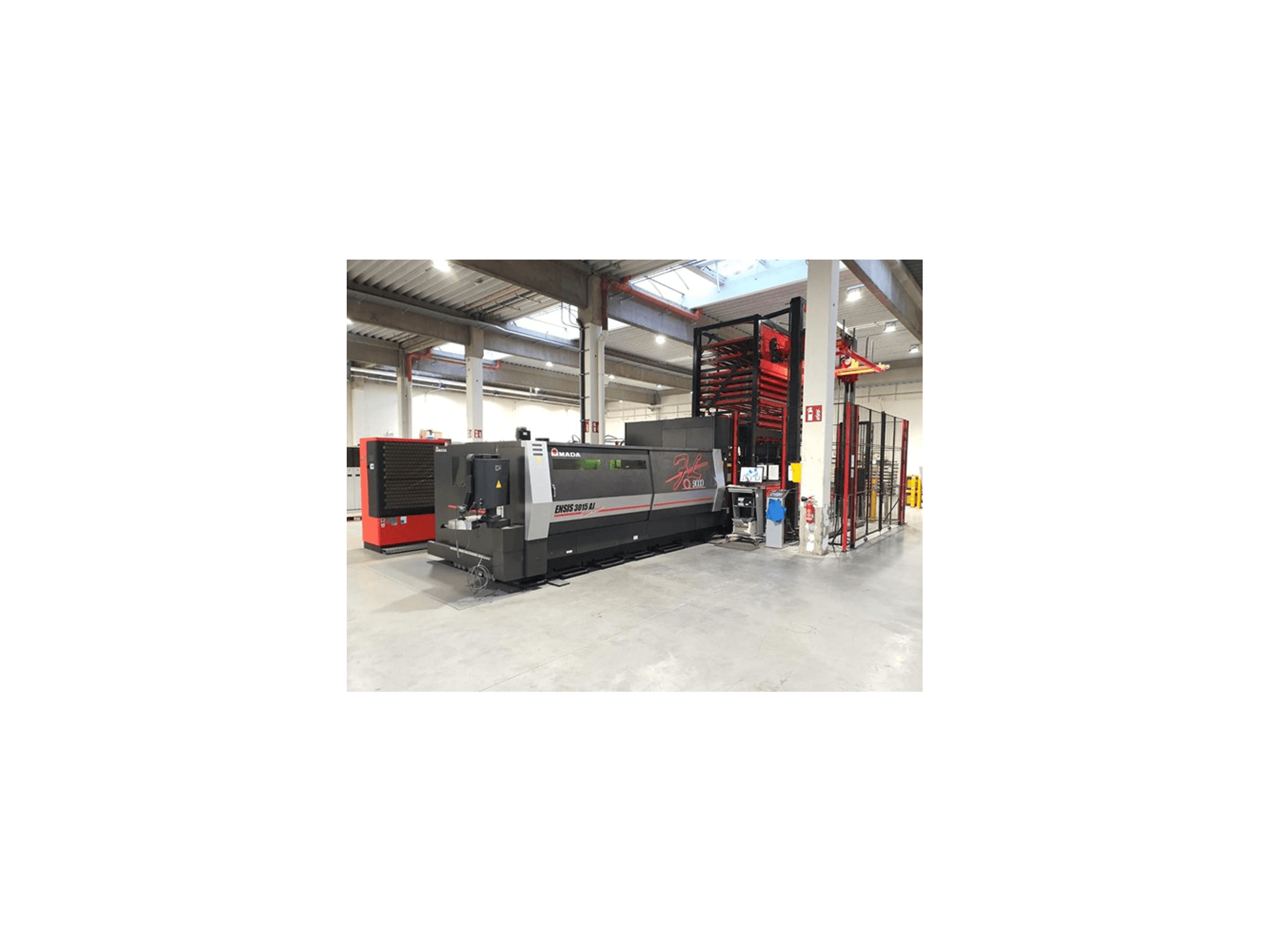 Станок лазерной резки Amada ENSIS 3015 Aj вид спереди, установленный в просторной промышленной мастерской с металлическими стеллажами.