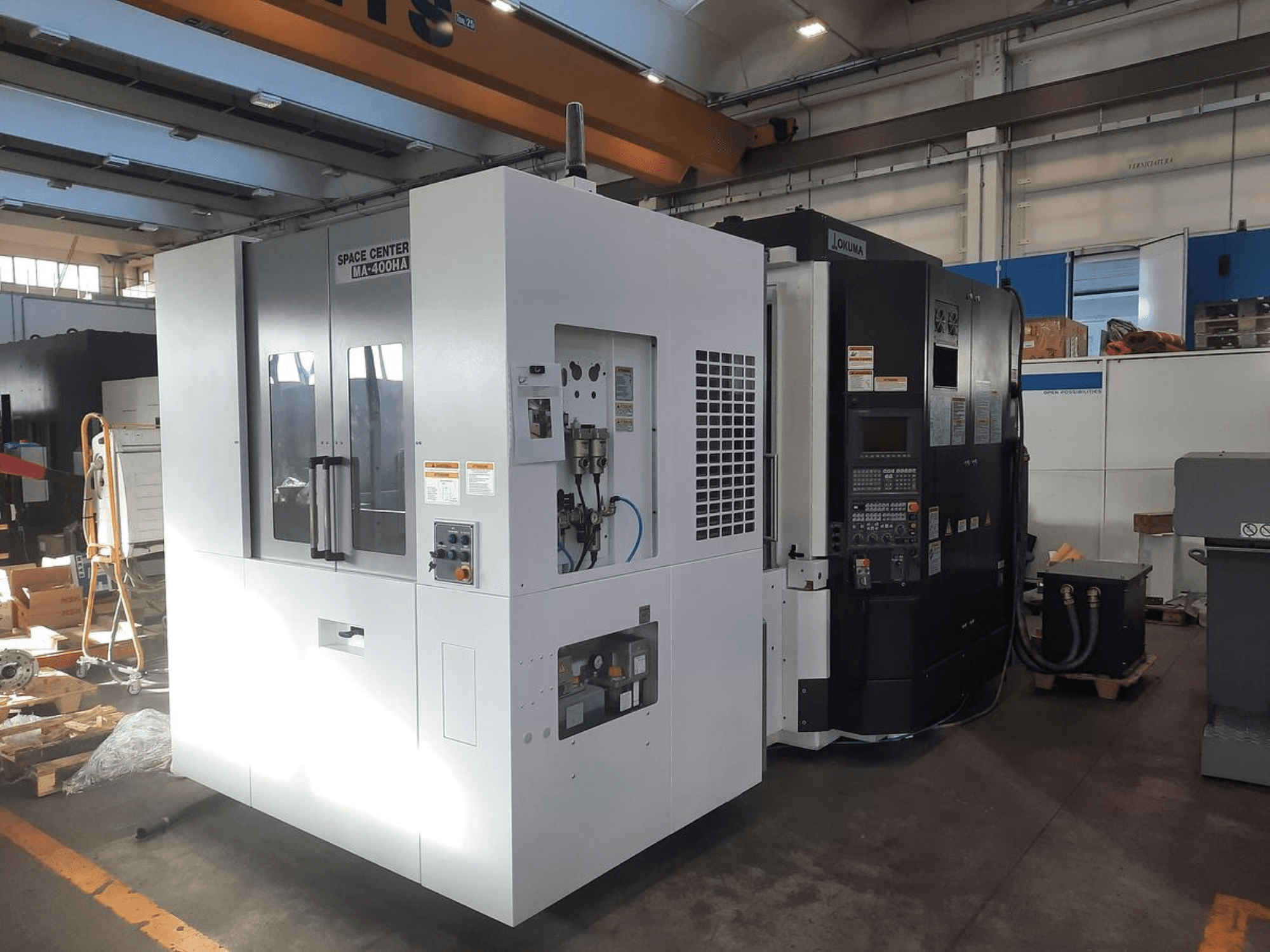 Вид спереди на станки с ЧПУ SPACE CENTER IM-400HAA и OKUMA, демонстрирующие различные элементы управления и наклейки производителей.