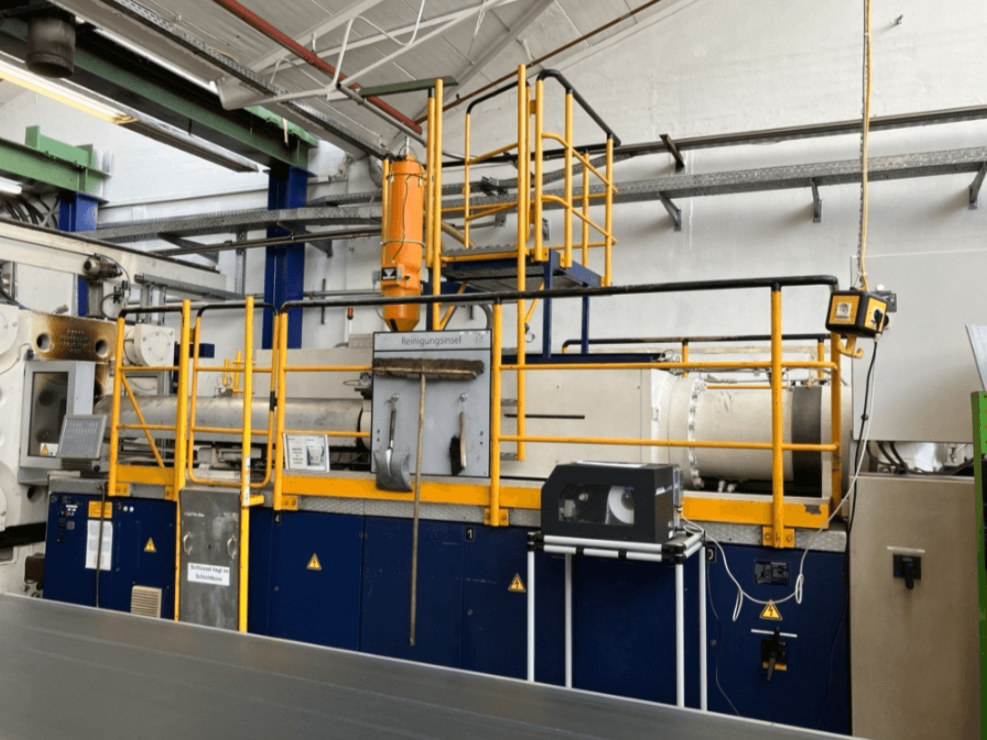 Гидравлический термопластавтомат Krauss Maffei 1000-8000 M, вид сбоку, видны защитные перила и панель управления.