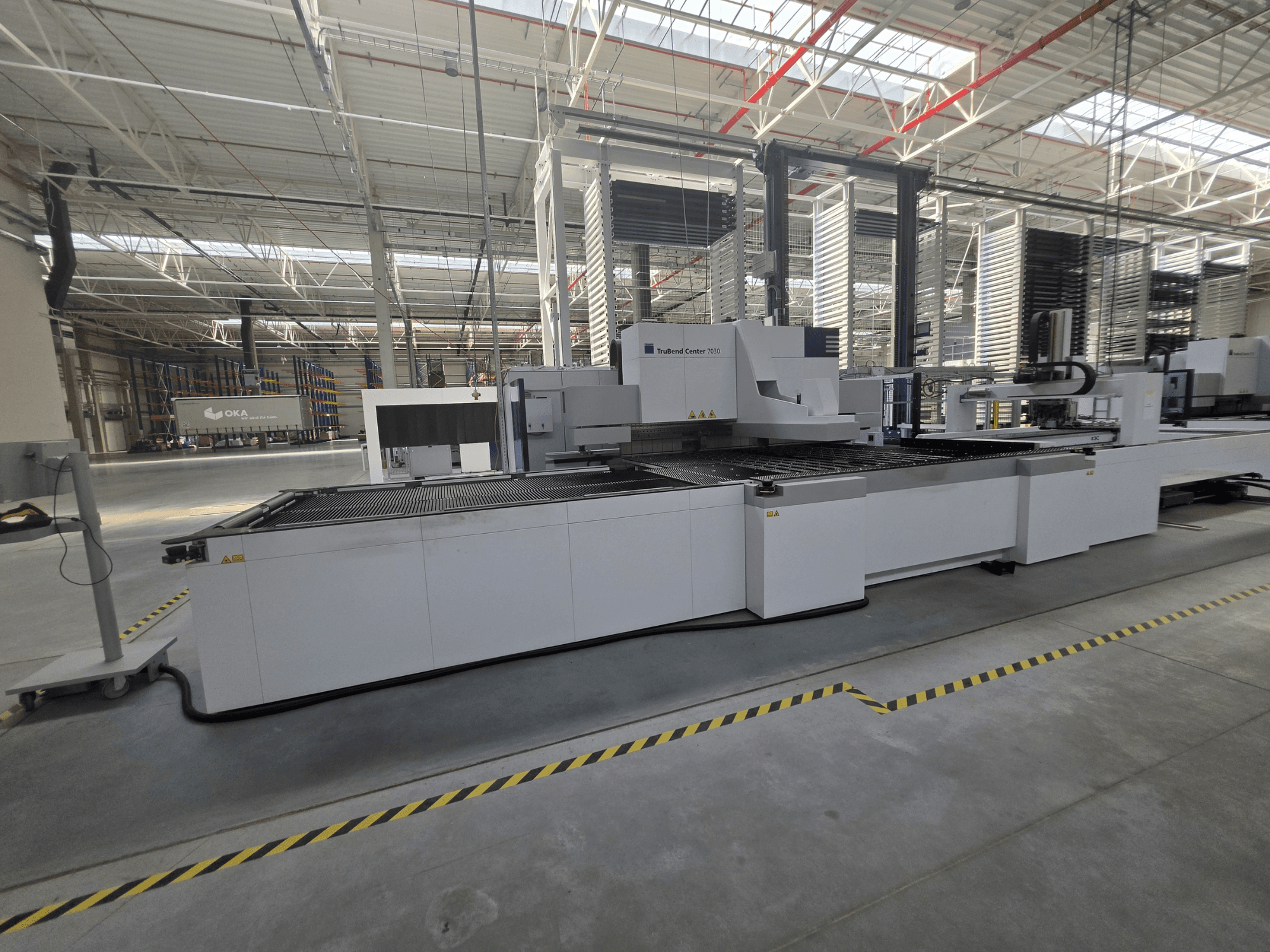 Гибочный станок TRUMPF TruBend Center 7030, вид сбоку, демонстрирующий рабочую зону и панель управления в просторном цехе.