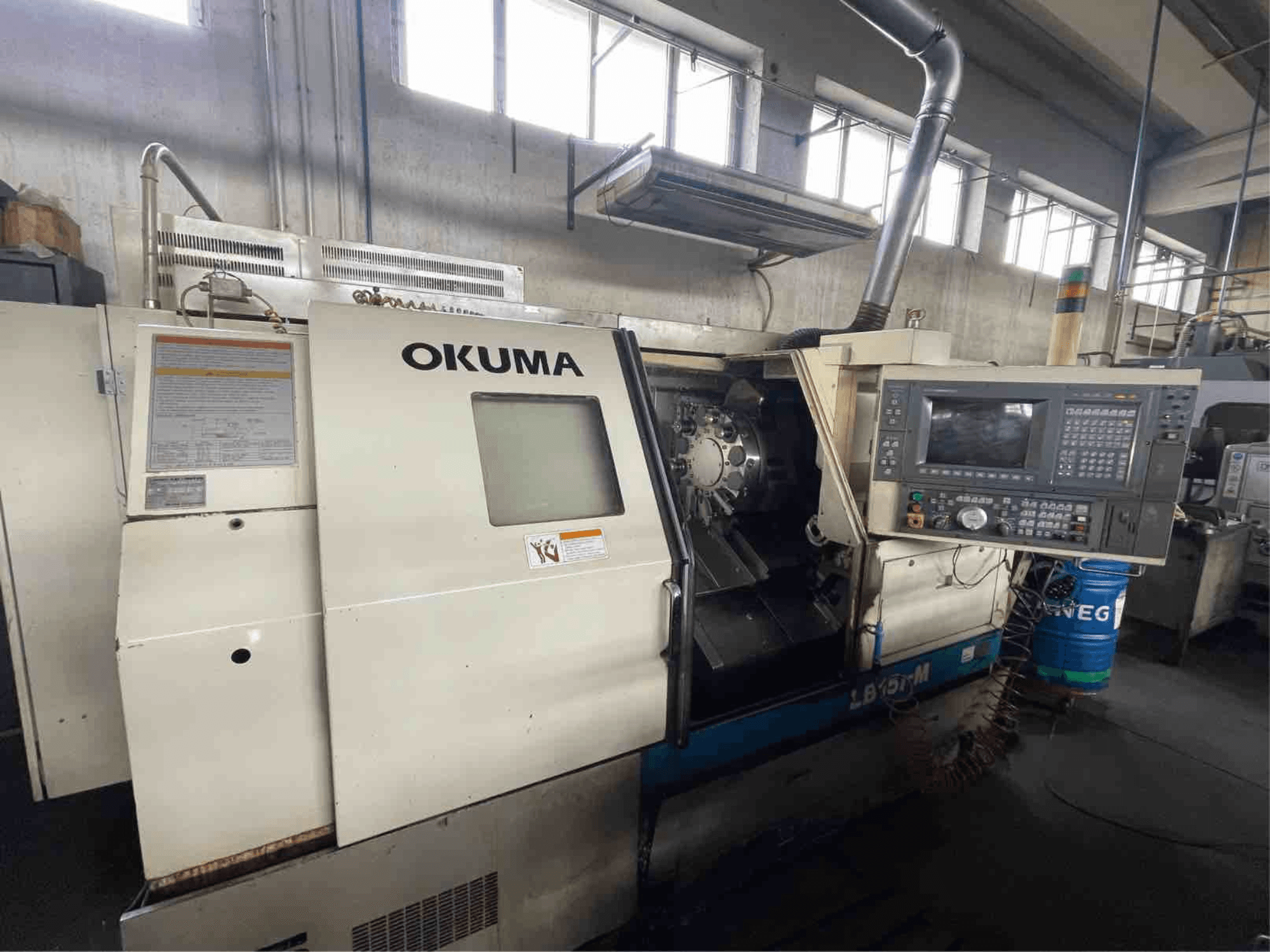Горизонтальный токарный станок Okuma LB15i-M, вид спереди; панель управления и зона режущего инструмента с подробными индикаторами.