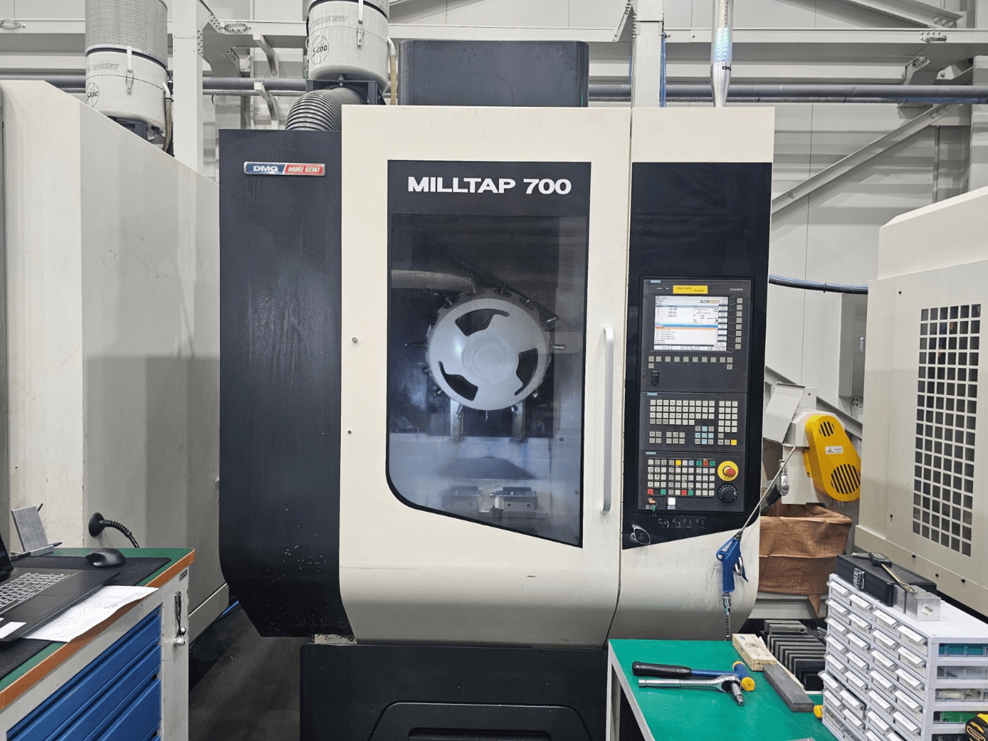 Вертикальный обрабатывающий центр DMG MORI MILLTAP 700, вид спереди, на котором видны панель управления, шпиндель и детали рабочей зоны.