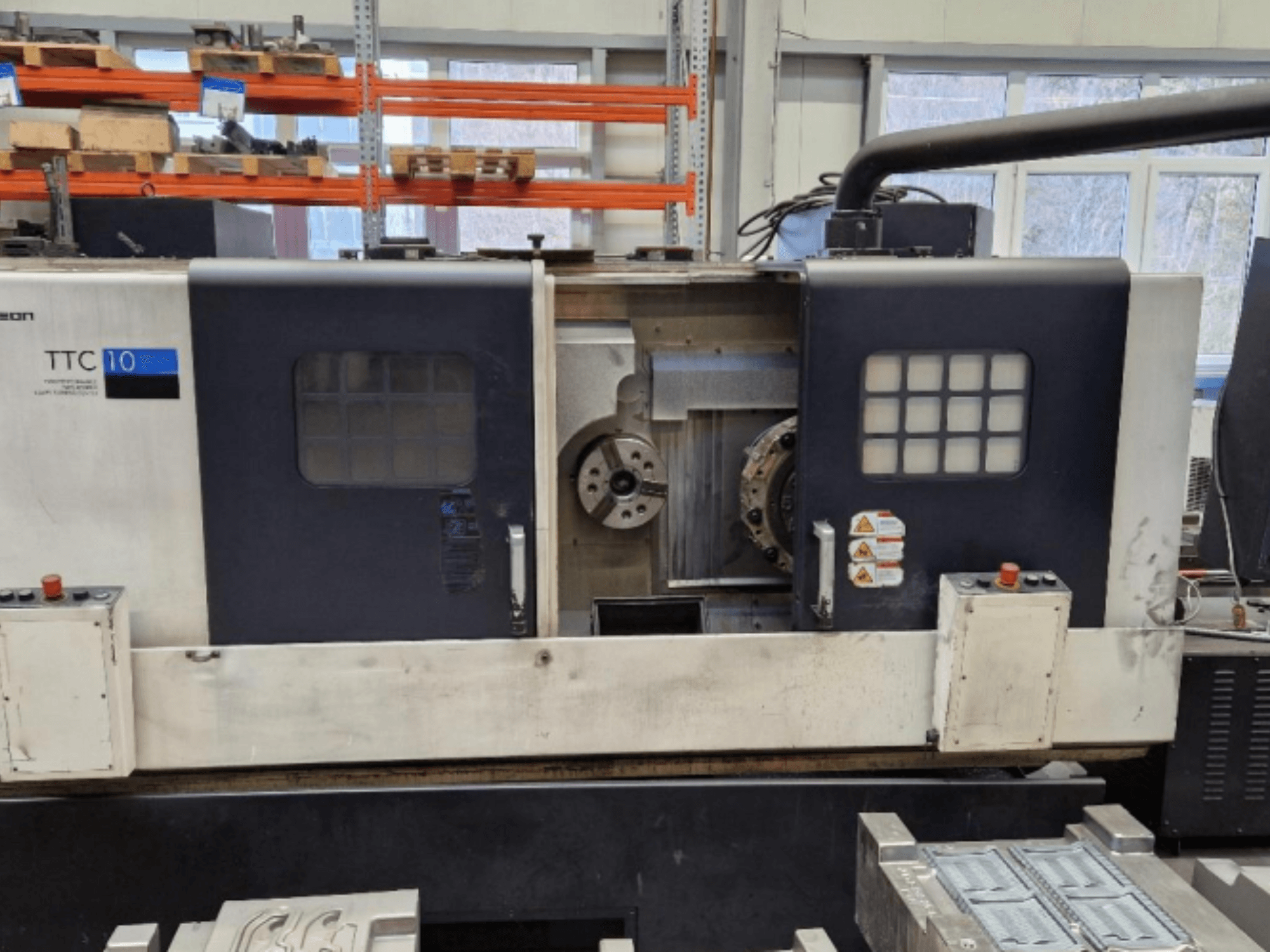 Вид спереди токарного станка TTC 10: панель управления, видимые патроны и рабочая область с металлическими деталями.