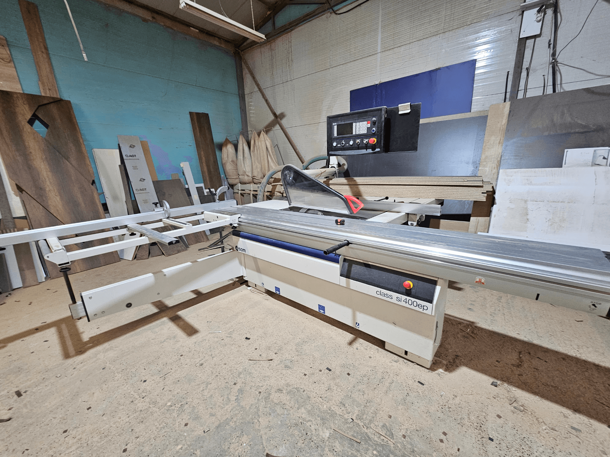 Пила для резки панелей класса SI400EP, вид спереди, с регулируемым ограждением, на песчаном полу мастерской, в окружении деревянных панелей.