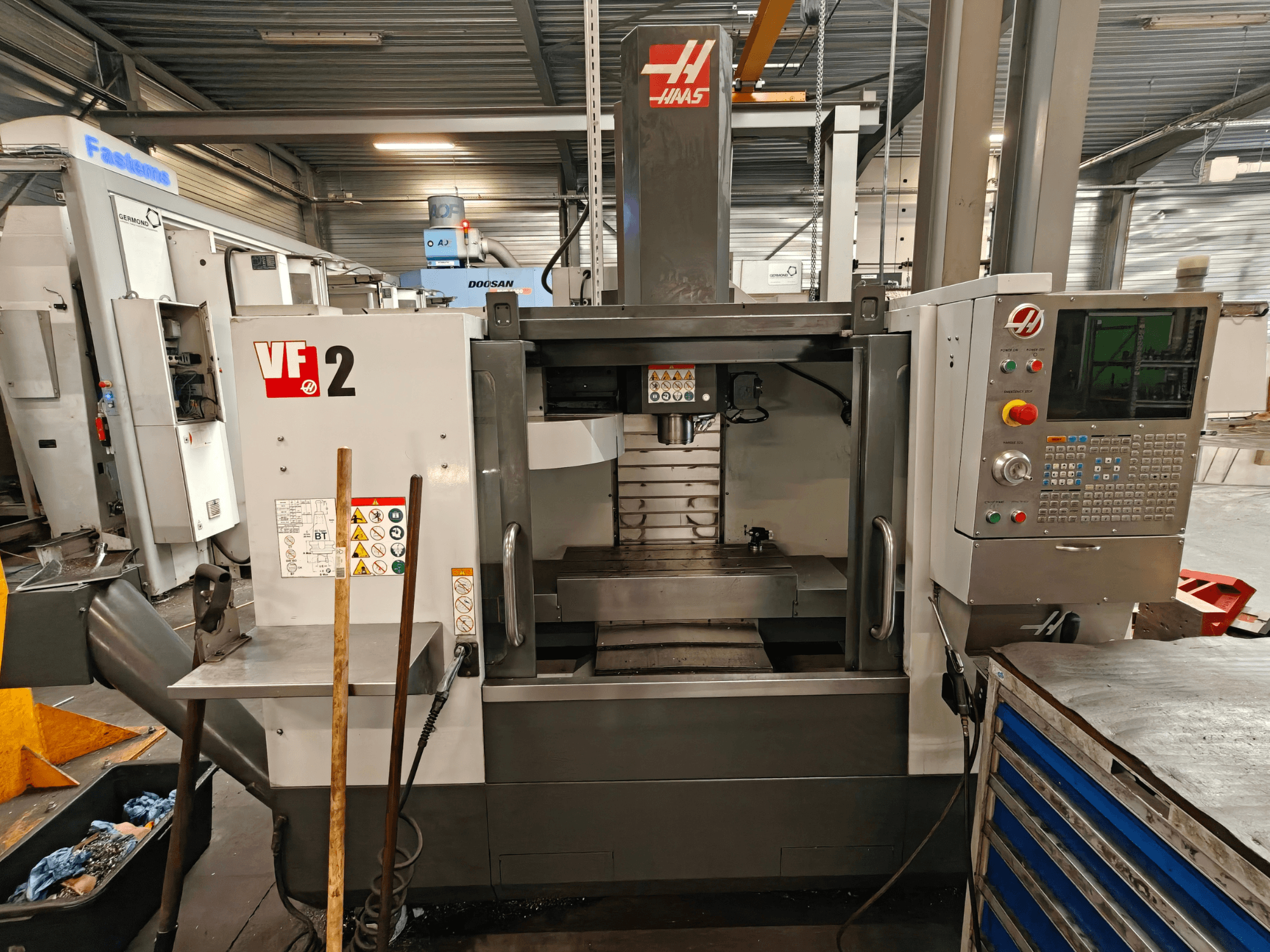 Вертикальный обрабатывающий центр HAAS VF-2, вид спереди, на котором видны элементы управления, шпиндель и рабочий стол в условиях цеха.