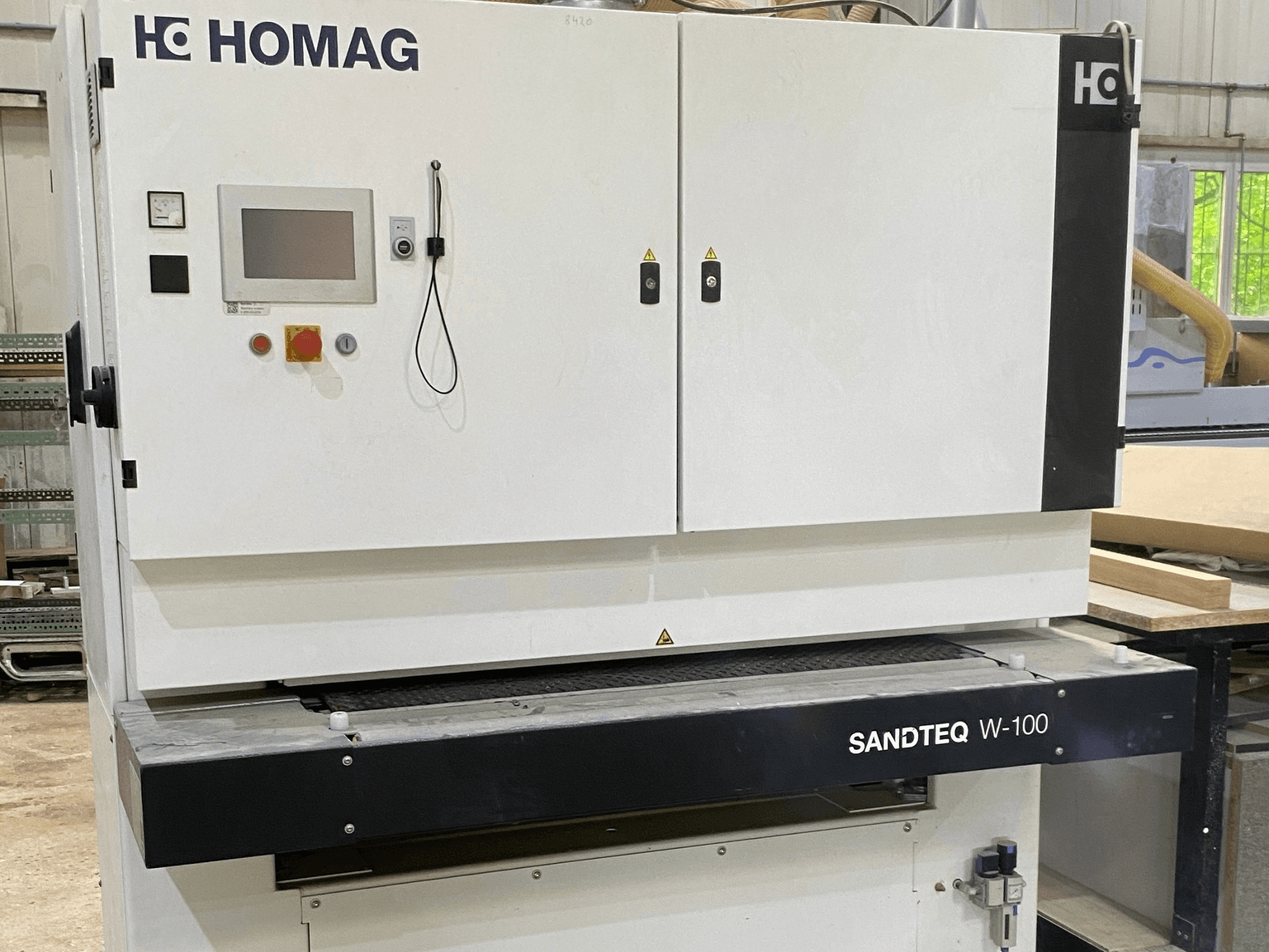 Ленточная шлифовальная машина HOMAG SANDTEQ W-100 в цеху: на снимке видны панель управления, патрубок для отвода пыли и зона шлифовальной ленты. Вид спереди.