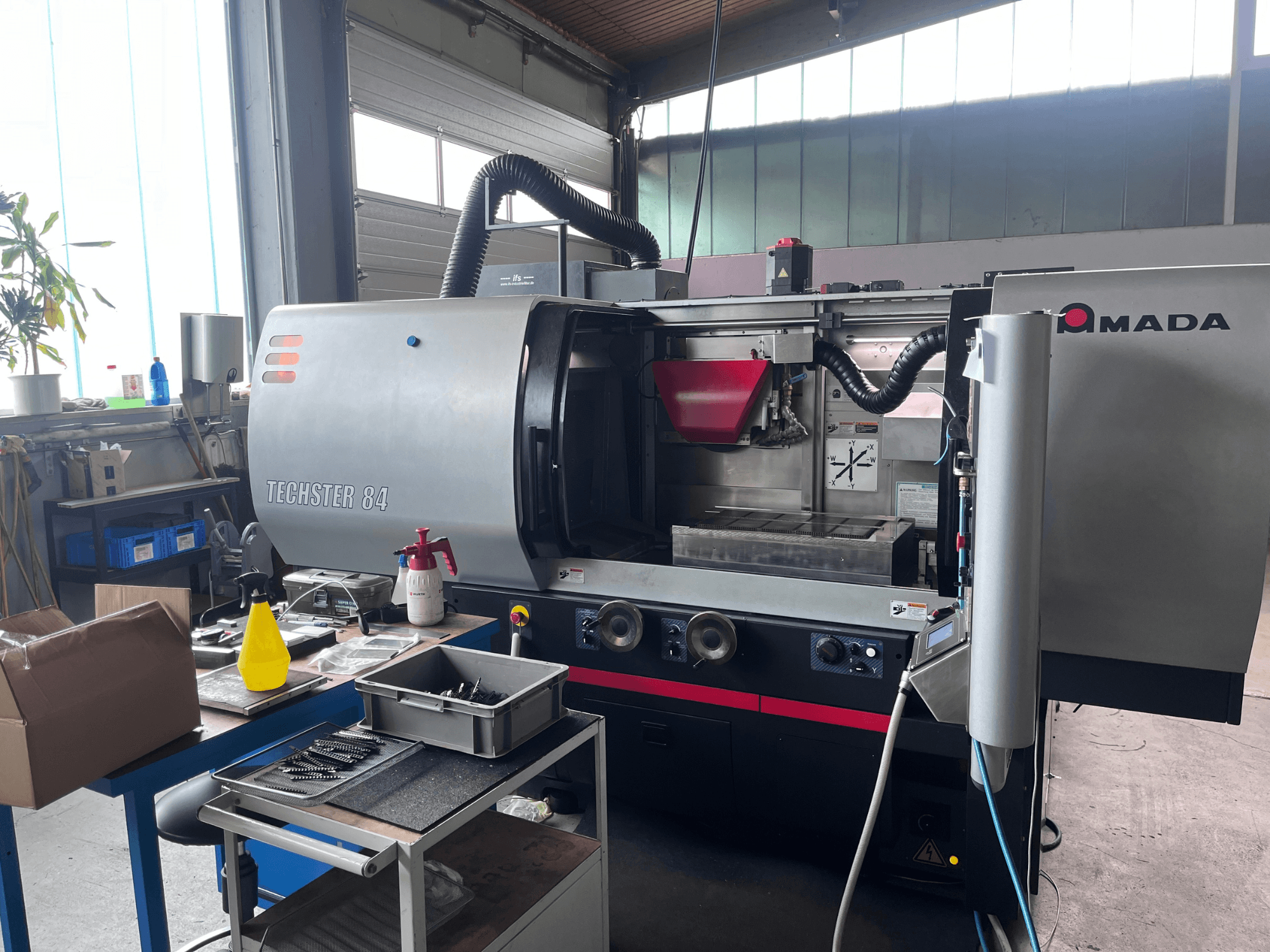 Плоскошлифовальный станок AMADA Techster 84 в цехе: вид спереди с органами управления и красным бункером.