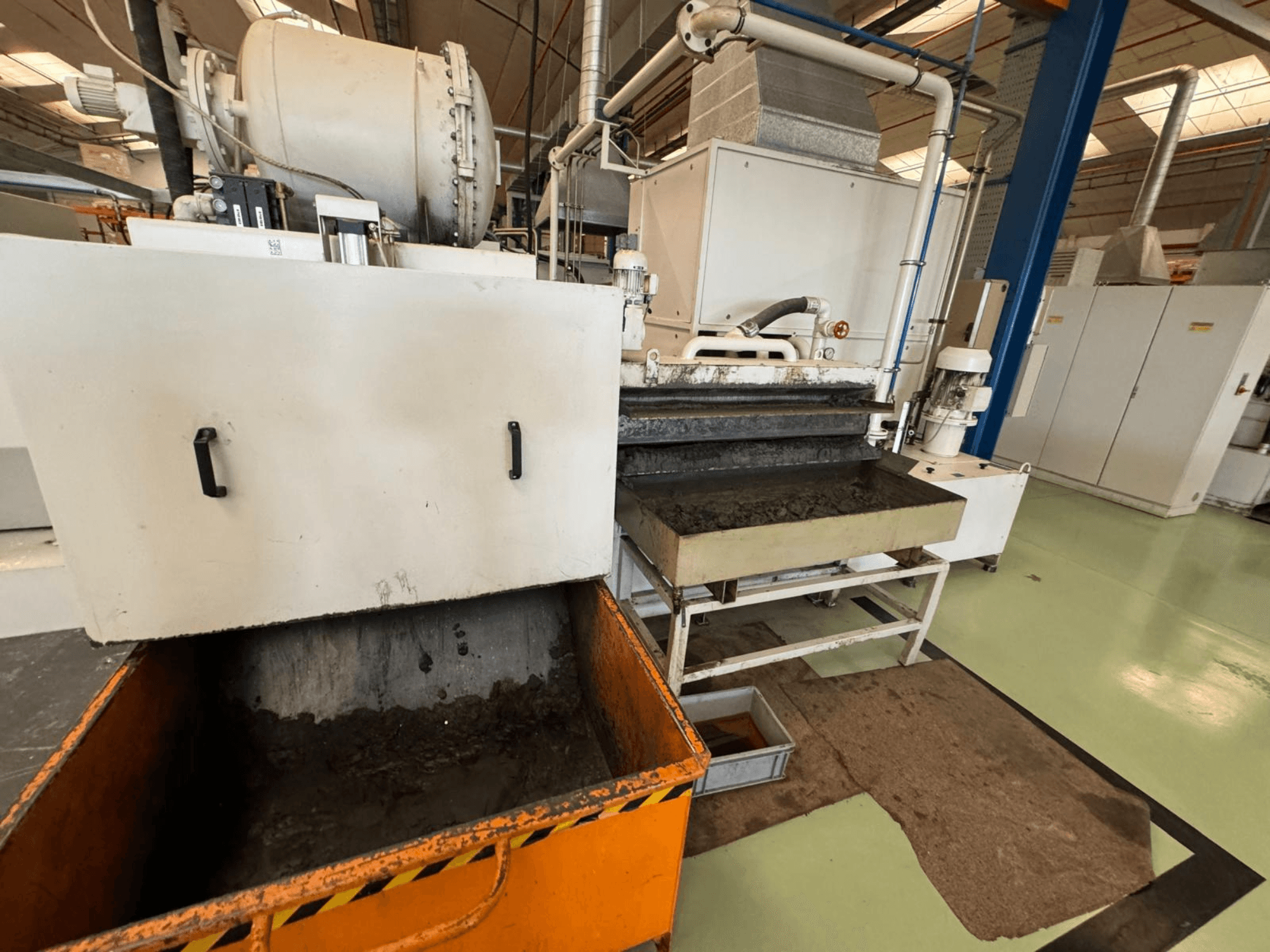 Промышленное технологическое оборудование с оранжевым контейнером для отходов, вид спереди; содержит двигатель, конвейеры и зону обслуживания.