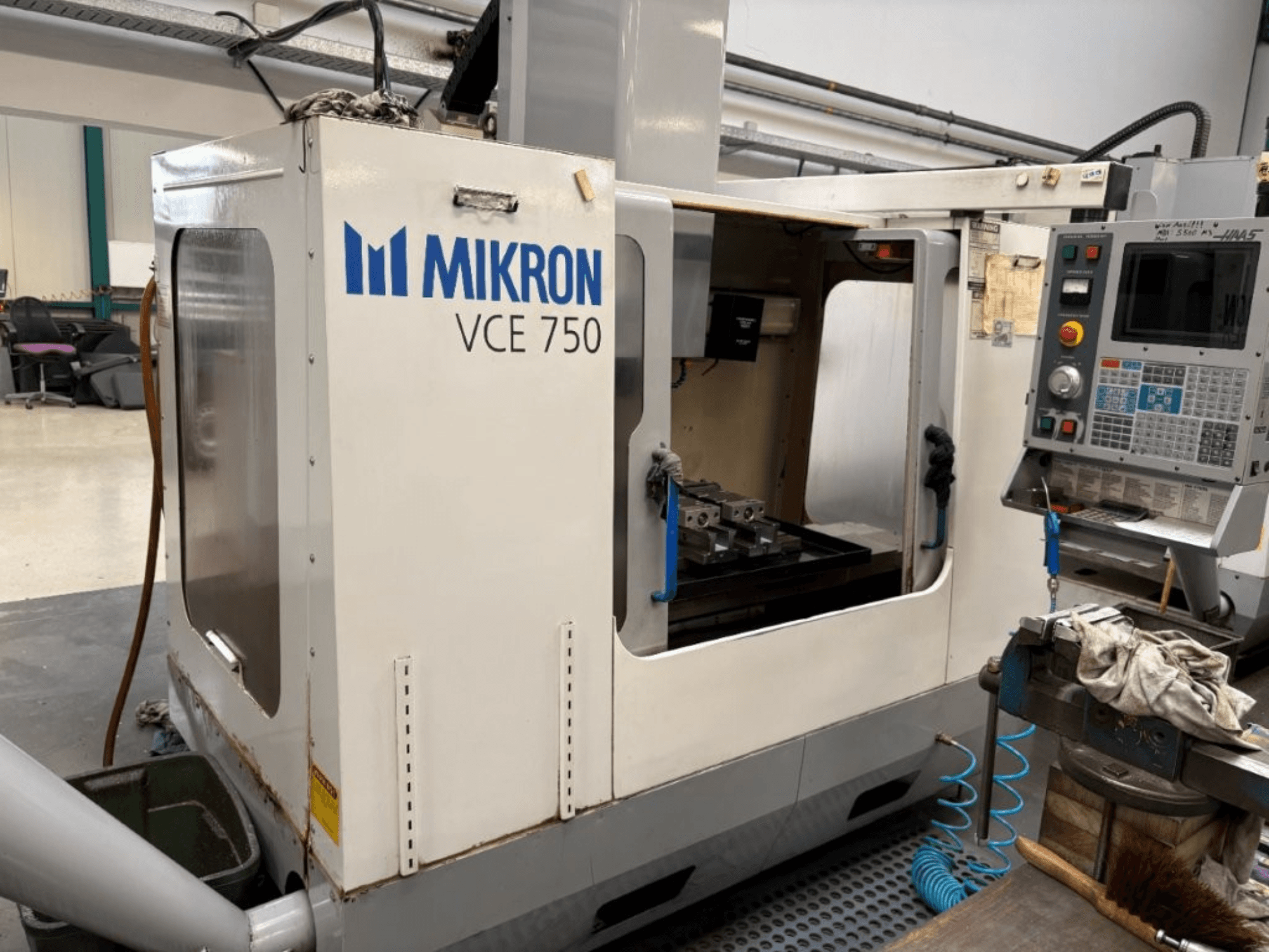 Фрезерный станок с ЧПУ Mikron VCE 750 с видом спереди, с обработанным рабочим столом и панелью управления с различными кнопками и экранами.