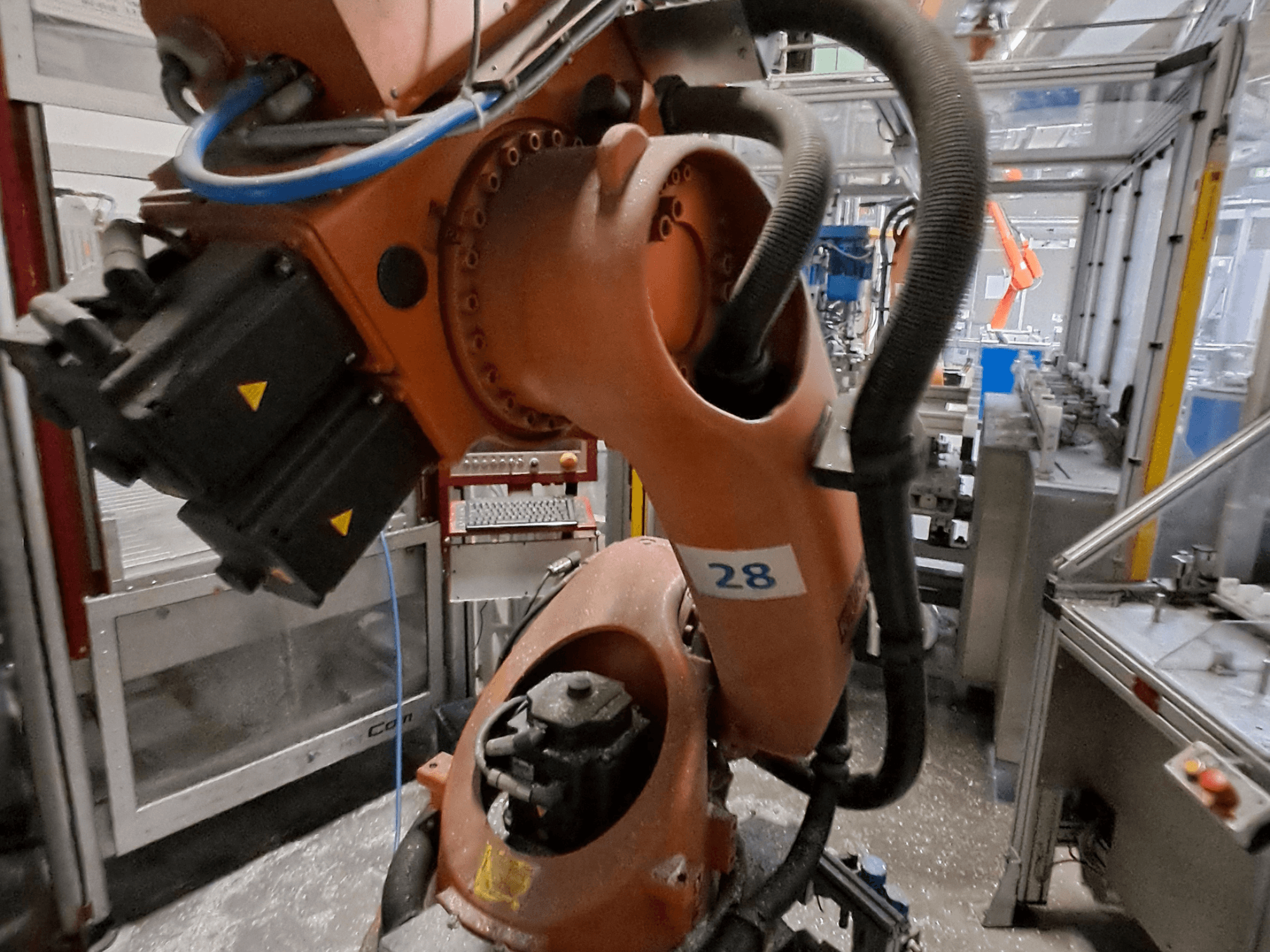 Крупный план манипулятора робота KUKA KR30-3 с оранжевым корпусом, пронумерованного цифрой 28, с видом сбоку, на котором видны двигатели и проводка.