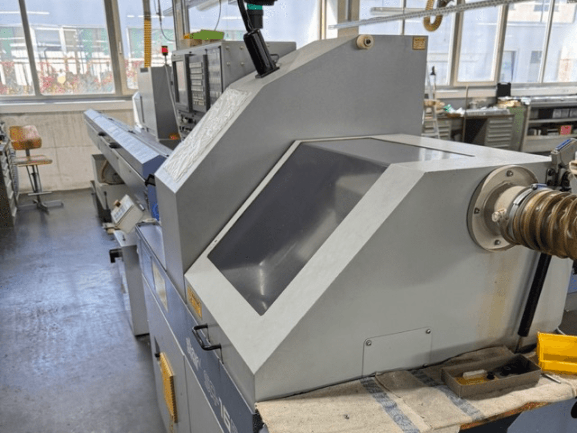 Серая промышленная машина, вид сбоку, имеет большую угловую панель, кнопки управления и насадку для шланга.