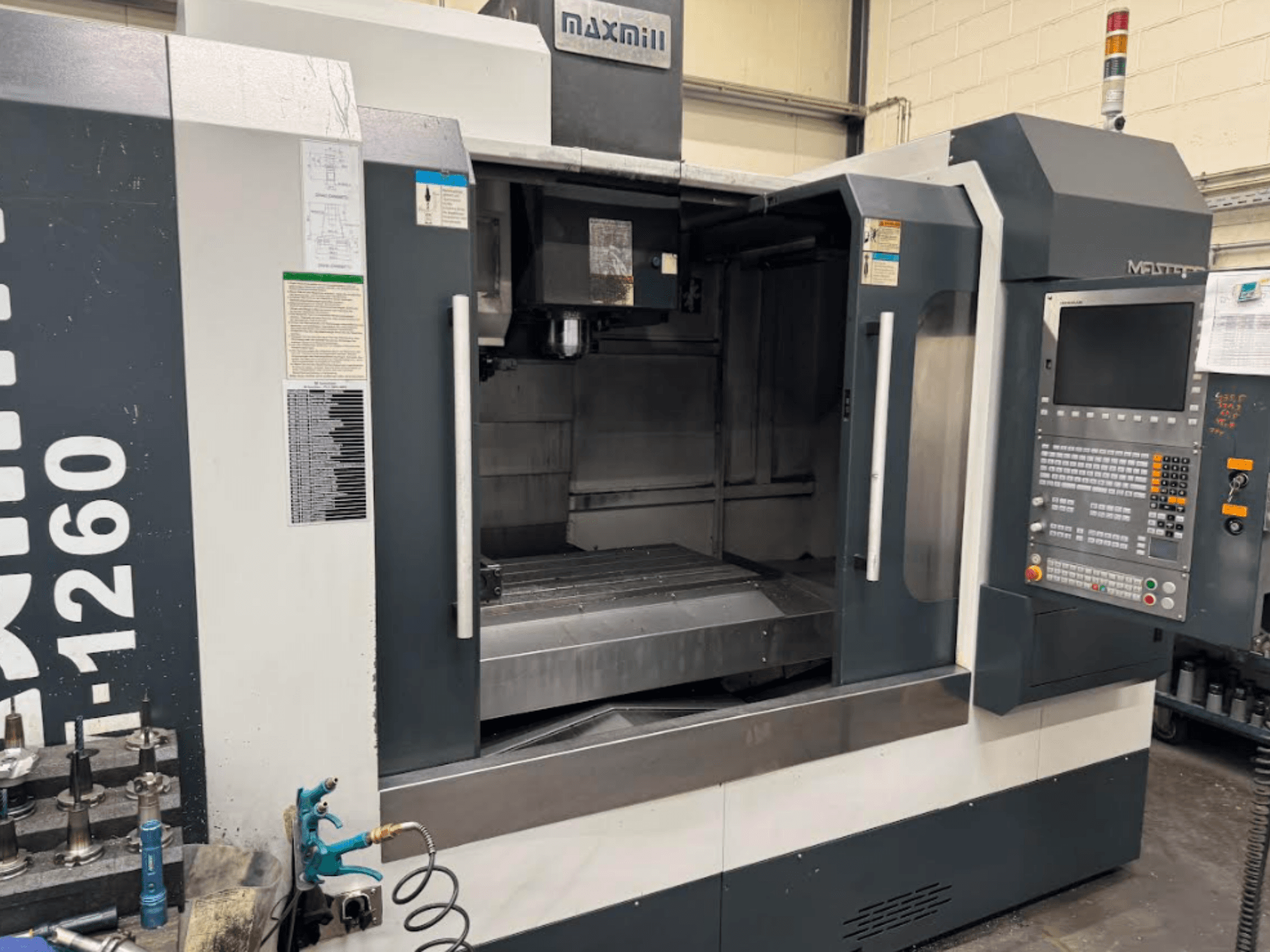Фрезерный станок с ЧПУ Maxmill, модель M-1260, вид спереди, показывающий пустую рабочую зону с панелью управления и инструкцией по эксплуатации.