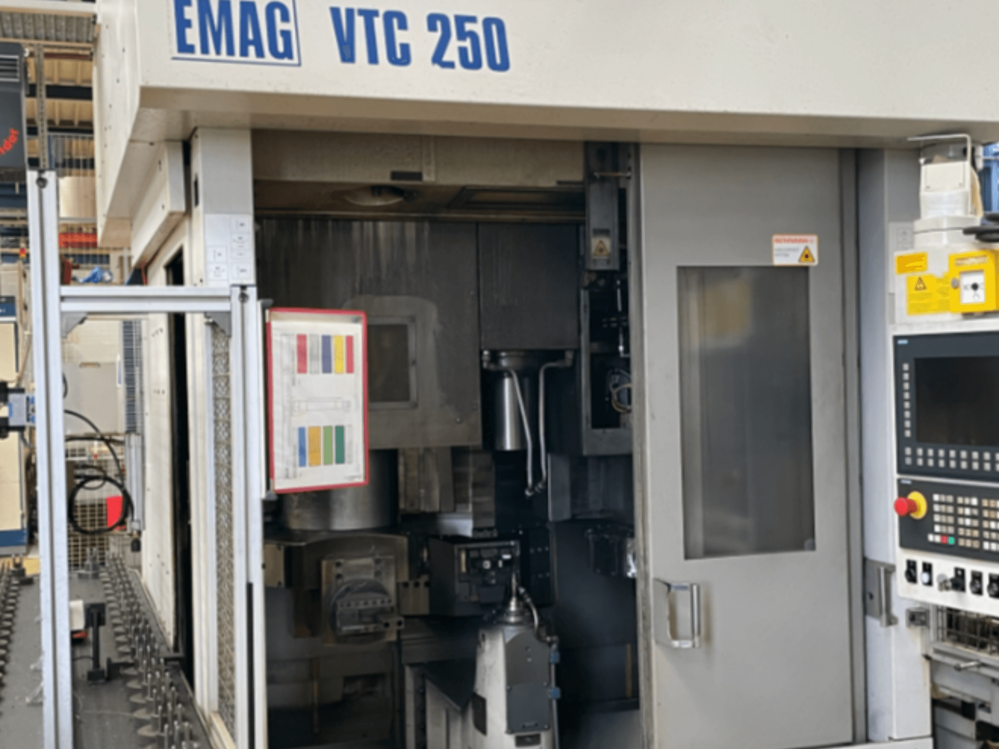 Вид спереди вертикального токарного станка EMAG VTC 250 с панелью управления, рабочим интерфейсом и открытой дверцей доступа.