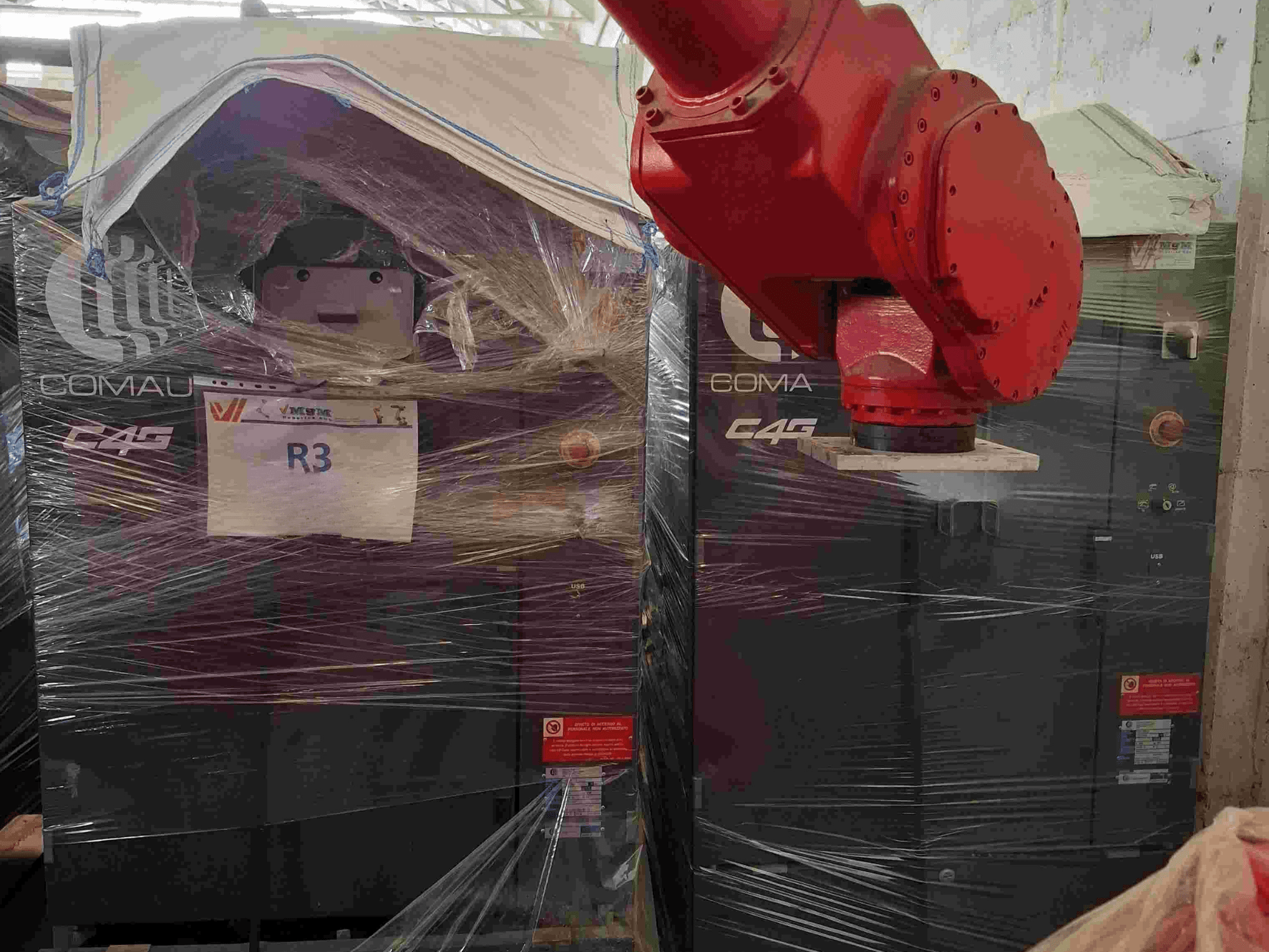 Роботизированная рука Comau C4G спереди, завернутая в пластик, с надписью "R3", на машине видны предупреждающие наклейки.