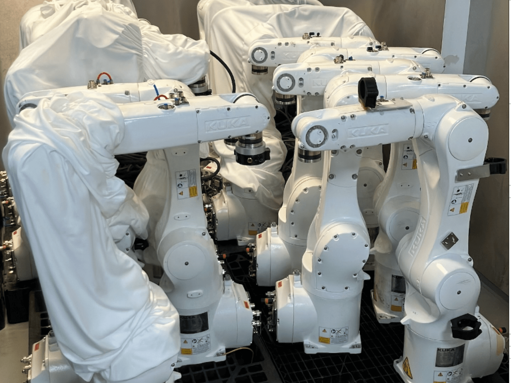 Роботизированные манипуляторы KUKA KR 10 R900-2, обтянутые белой тканью, вид сверху, несколько единиц на складе.