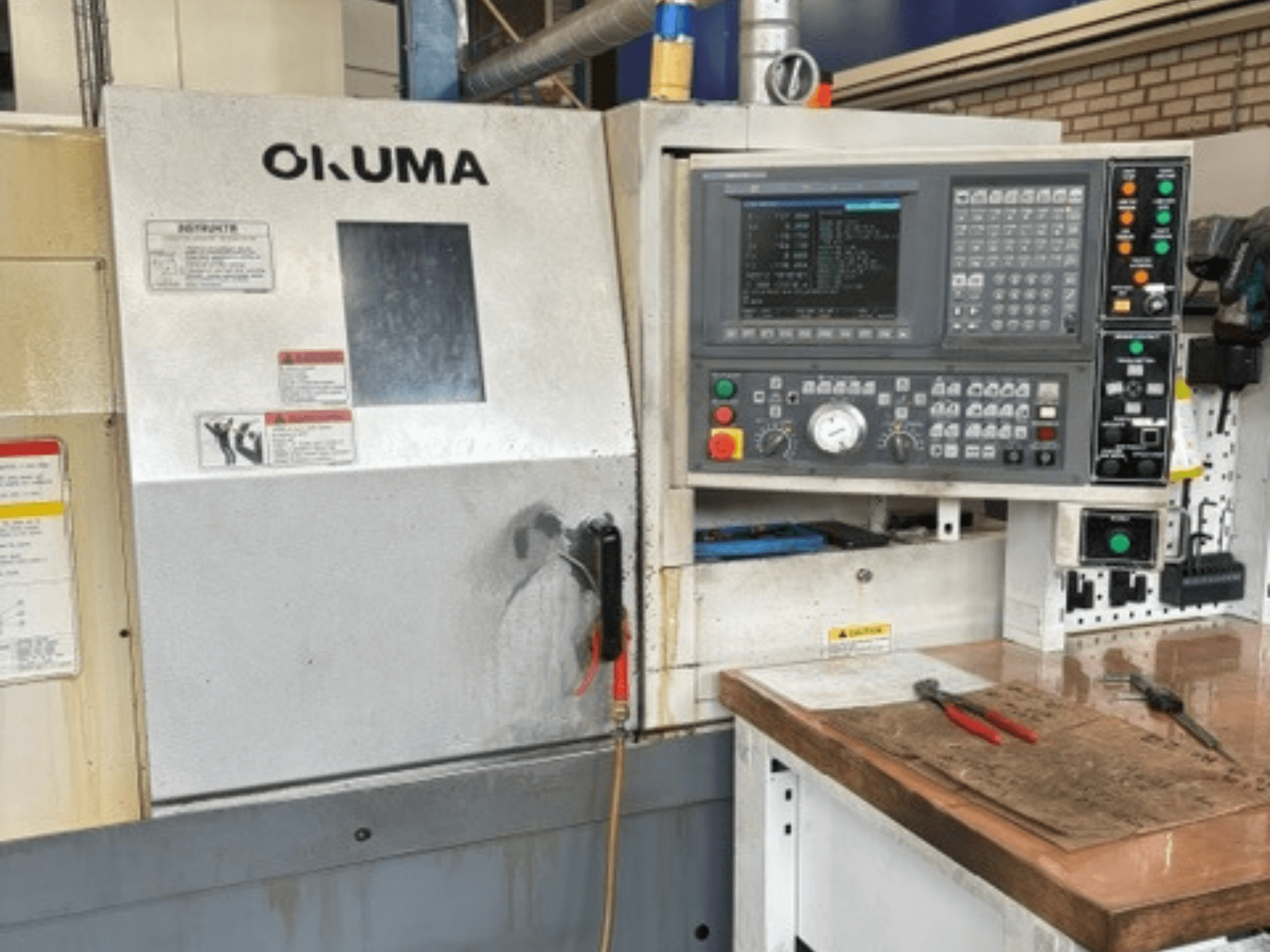 Горизонтальный токарный станок Okuma ES-L10II, вид спереди, с панелью управления, дисплеем и рабочей зоной с инструментами.