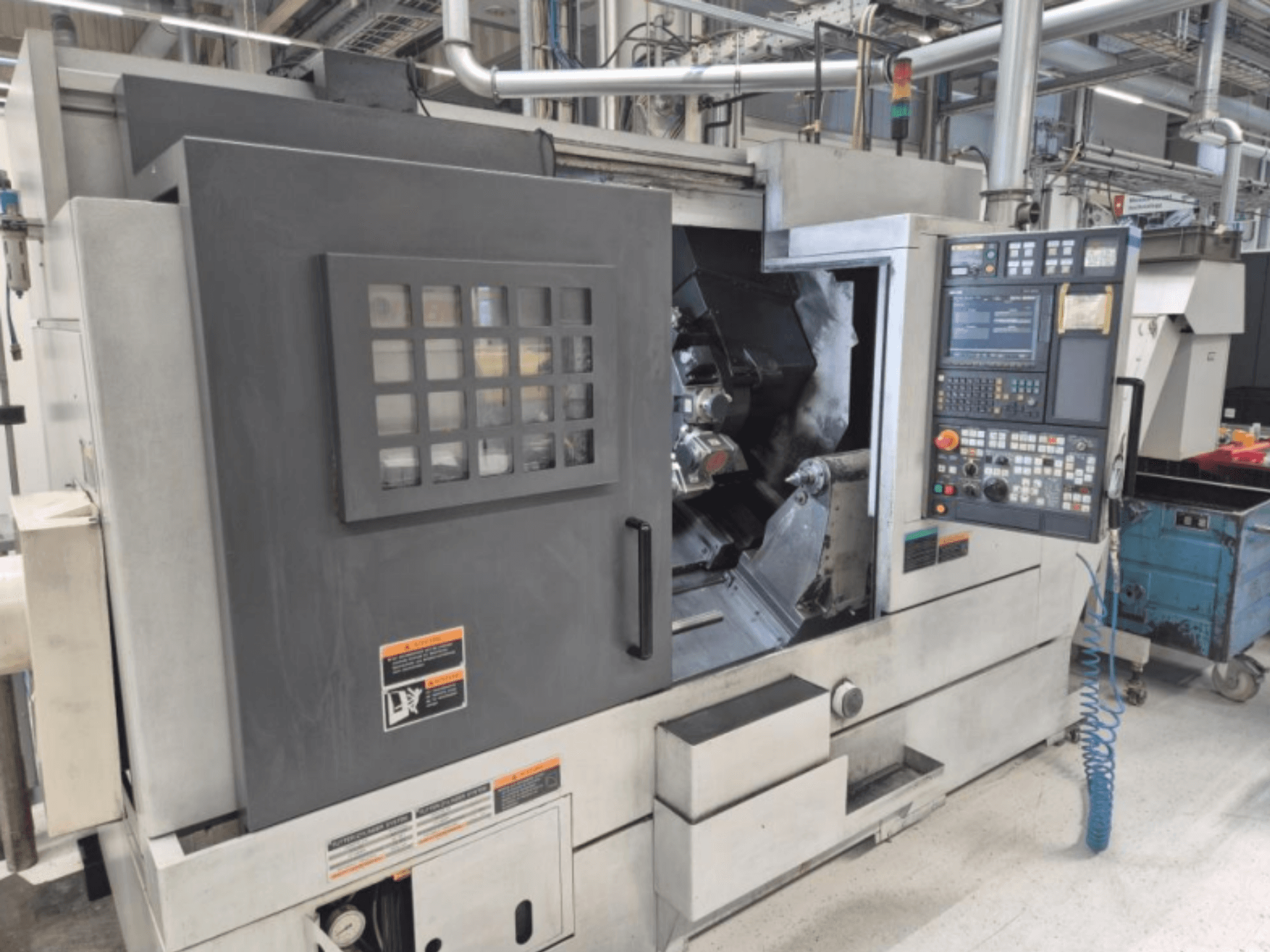 Токарный станок с ЧПУ с панелью управления, вид спереди. Имеет видимую рабочую зону и защитное окно, марка неизвестна.