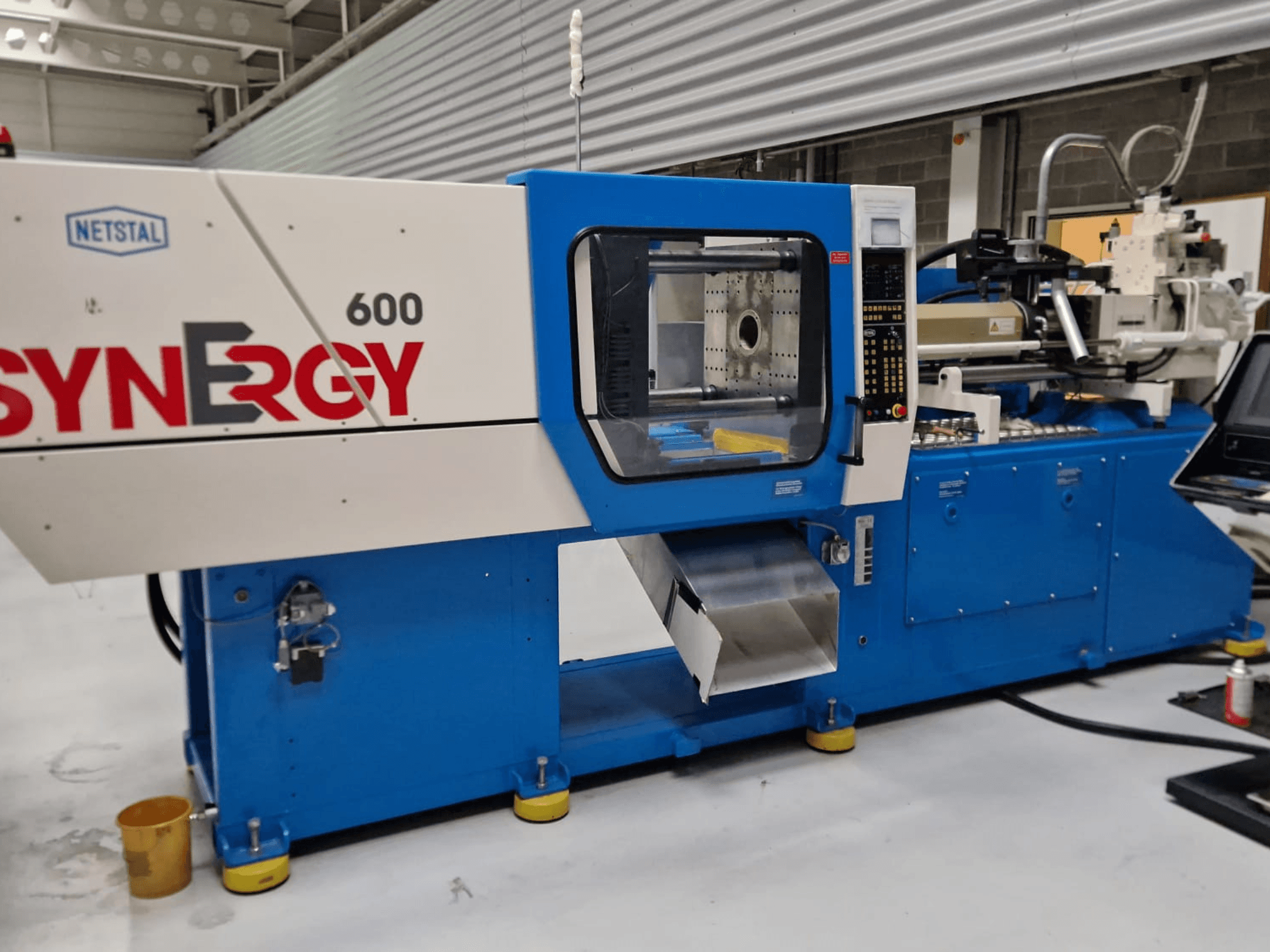 Гидравлическая машина для литья под давлением Netstal Synergy 600-230, вид сбоку, показывающий панель управления и зону впрыска.