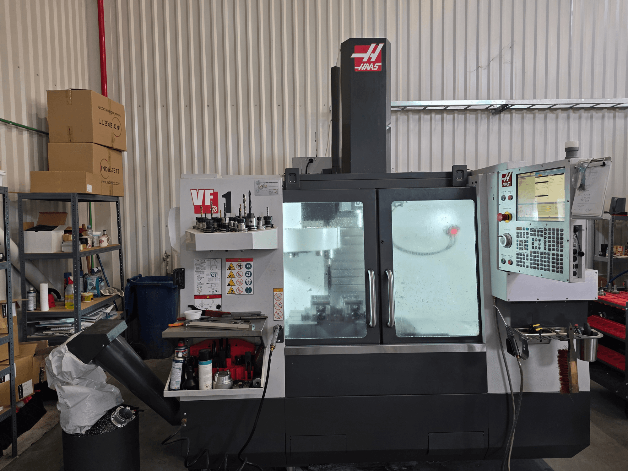 Вертикальный обрабатывающий центр HAAS VF 1 в мастерской, вид спереди, демонстрирующий панель управления и зону фрезерования с инструментами.
