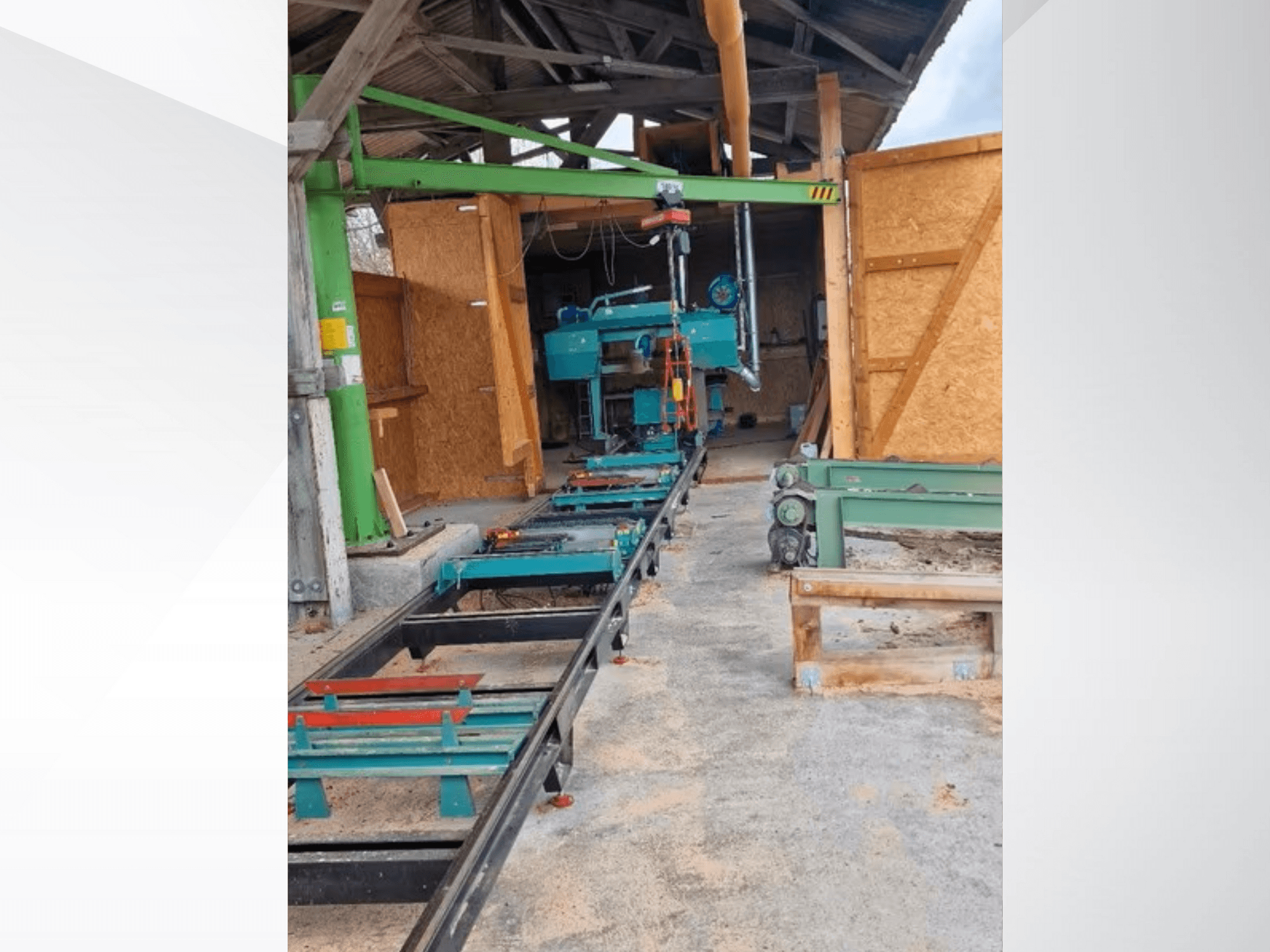 Горизонтальный ленточнопильный станок в мастерской, вид спереди. В комплект поставки входит рельсовый путь и дополнительные зеленые аксессуары.