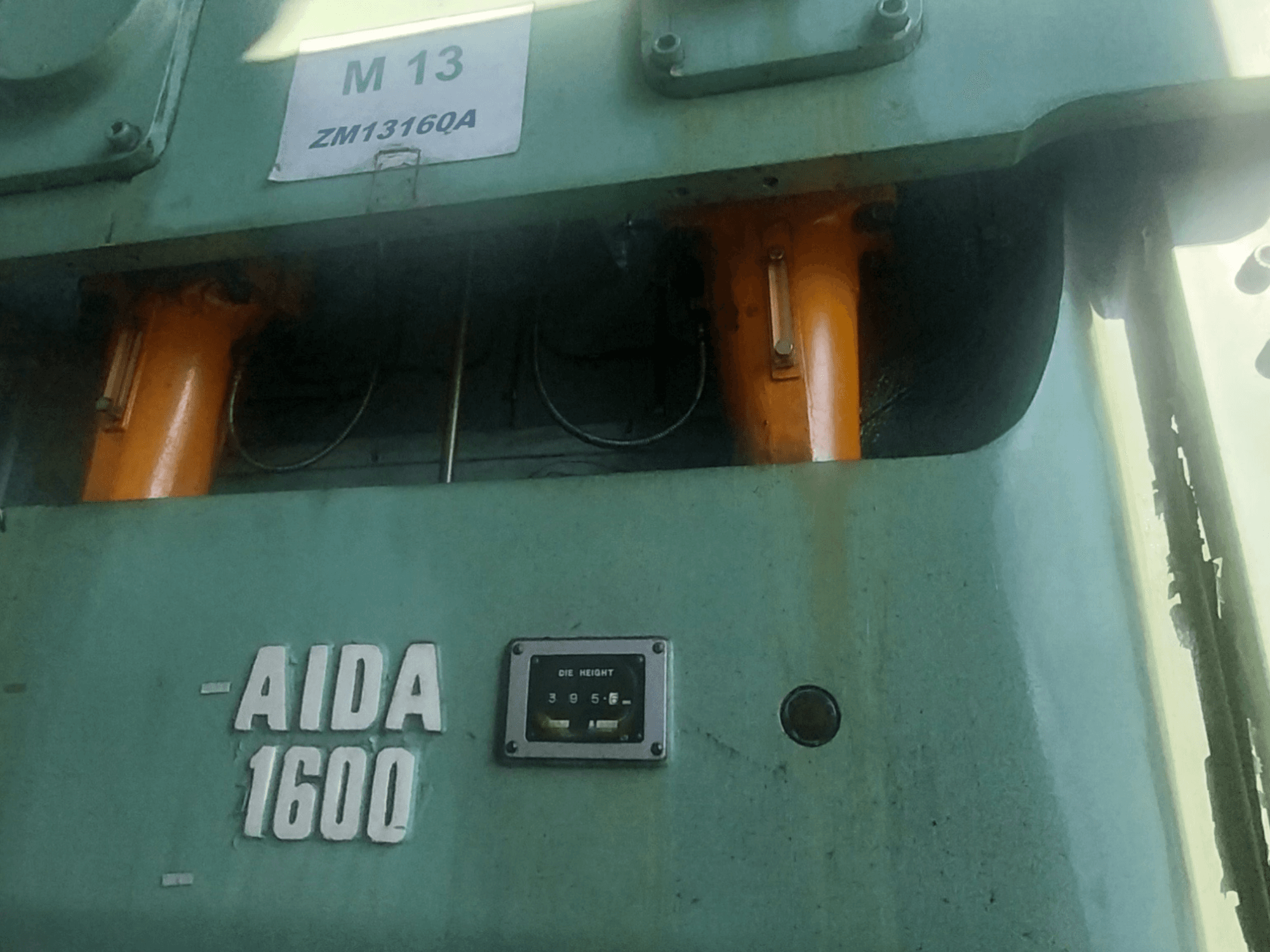 Механический штамповочный пресс AIDA NC2-1600, вид спереди; видны оранжевые гидравлические компоненты и измеритель высоты штампа.