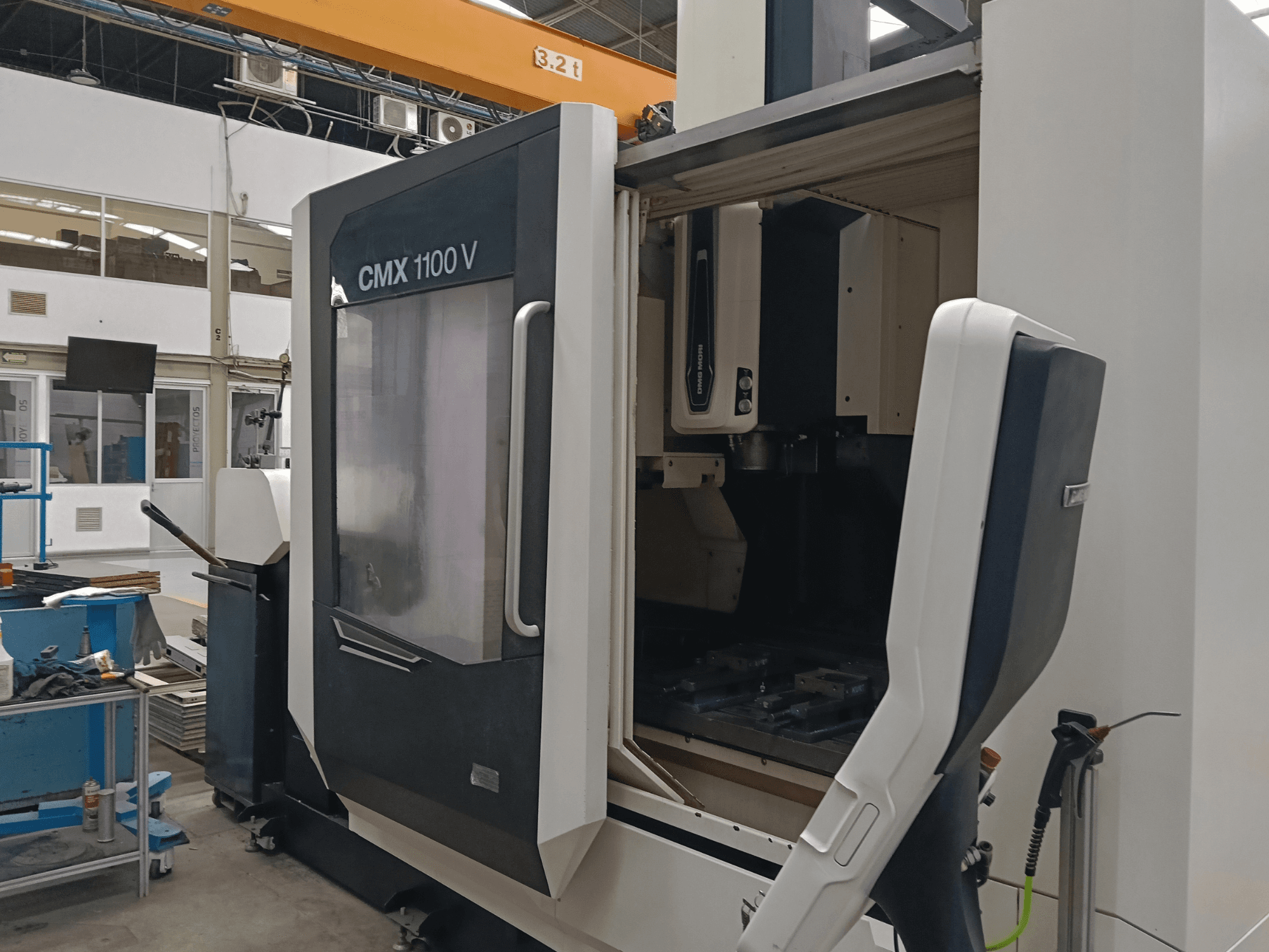 Вертикальный обрабатывающий центр DMG MORI CMX 1100 V, вид спереди с открытой дверью и внутренней компоновкой инструментов в промышленном помещении.
