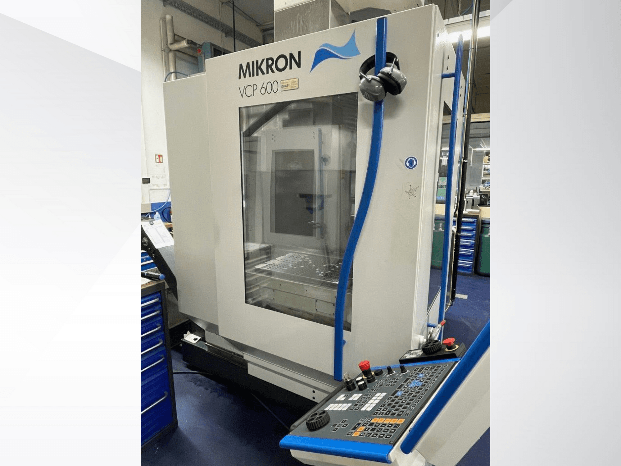 Обрабатывающий центр Mikron VCP 600 в мастерской, вид спереди, с панелью управления с кнопками и ручками.
