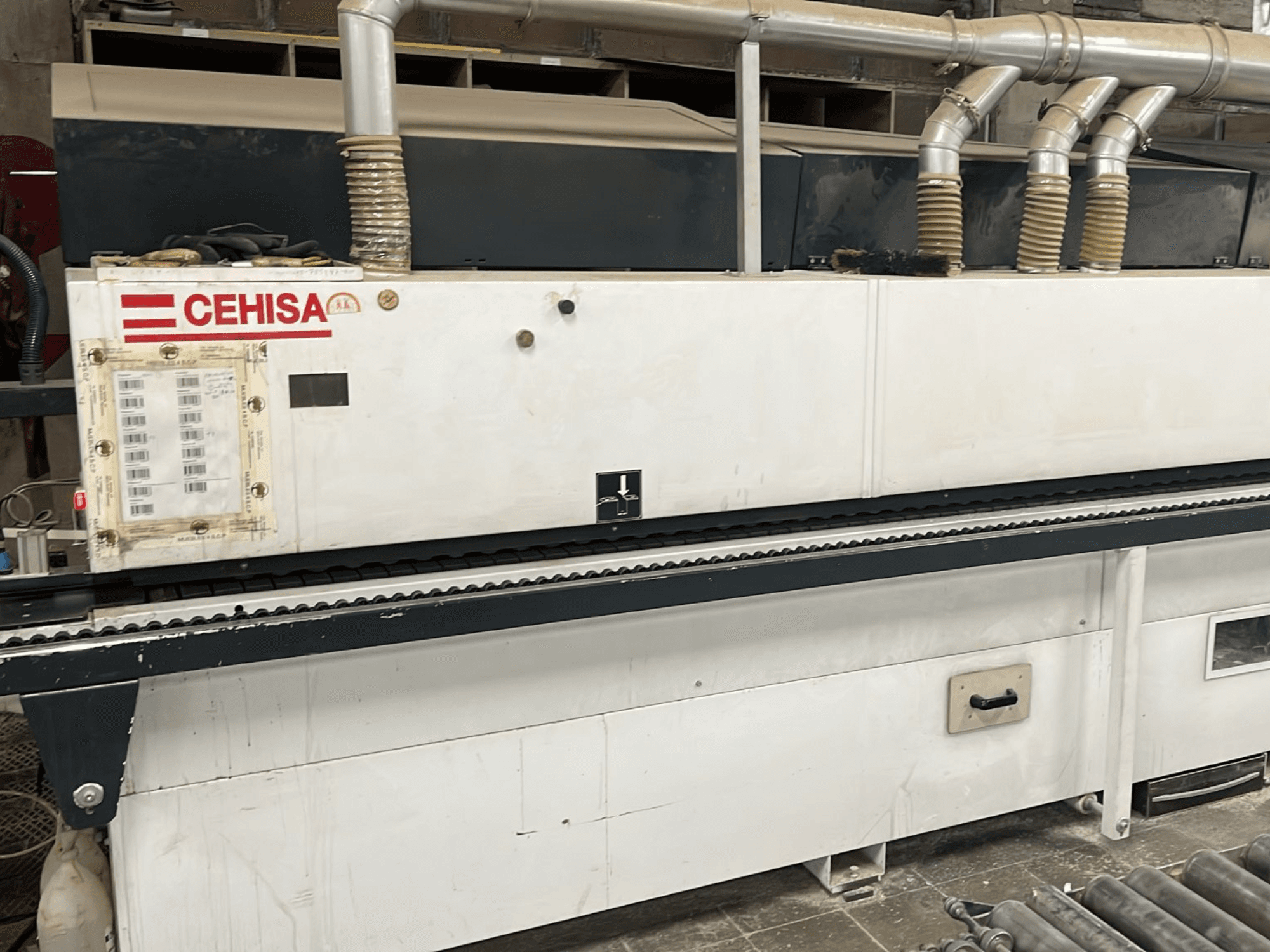 Кромкооблицовочная машина CEHISA PRO 12 CONCEPT, вид спереди, с панелью управления, трубами для отвода пыли и конвейерной лентой.
