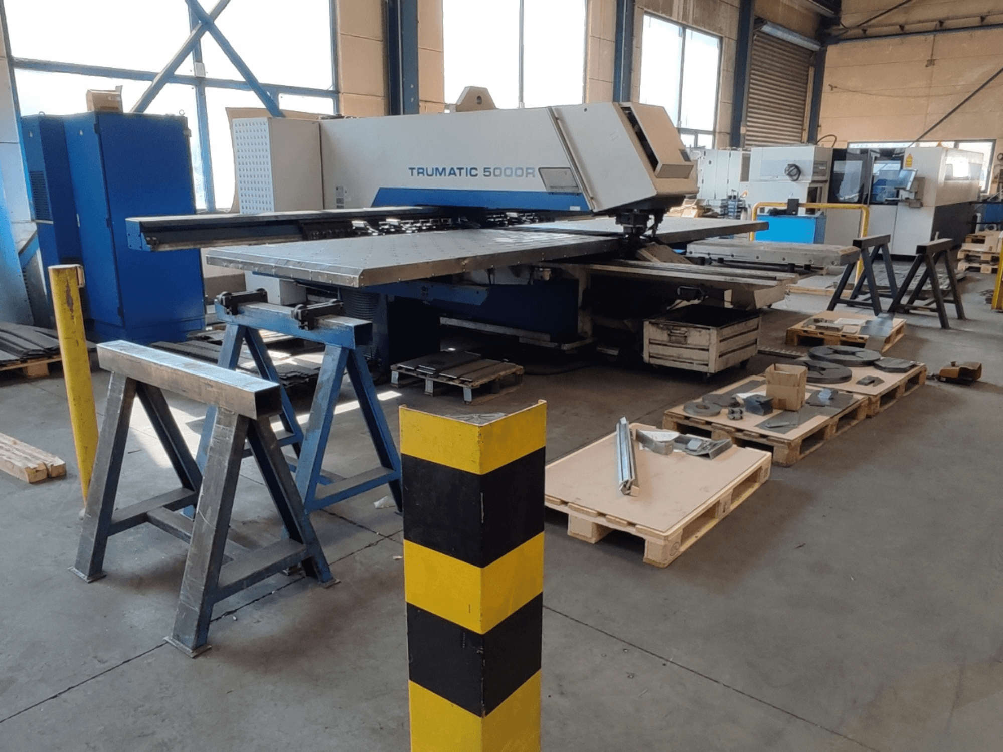 Штамповочный станок с ЧПУ TRUMPF Trumatic 5000 R в цехе, вид сбоку; рядом на поддонах — инструменты и материалы.